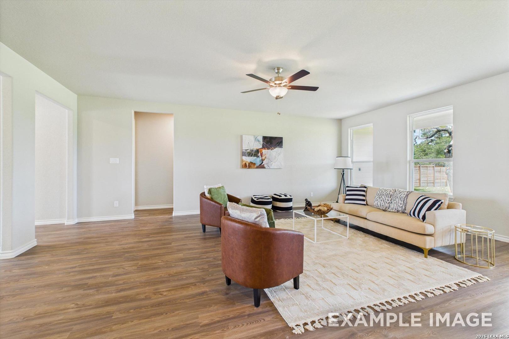Bright, open-concept living room with wood-style flooring in The Foster F floor plan at Potranco Oaks, Castroville, Texas.