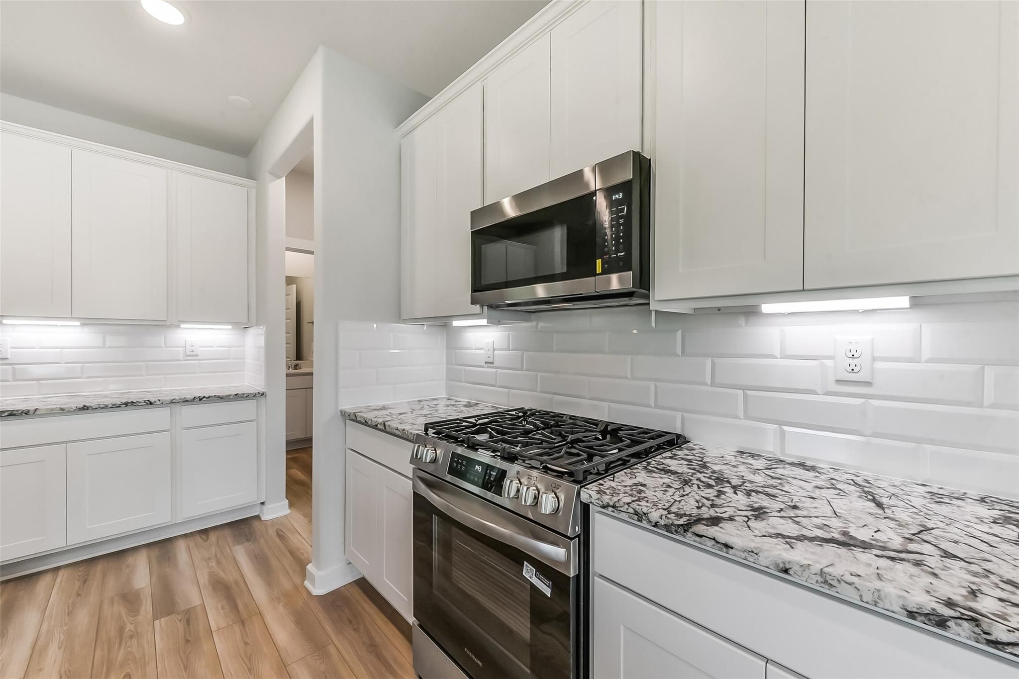 Modern white shaker kitchen with granite countertops, stainless steel gas range, subway tile backsplash in Davidson Homes The Frio G, Magnolia TX