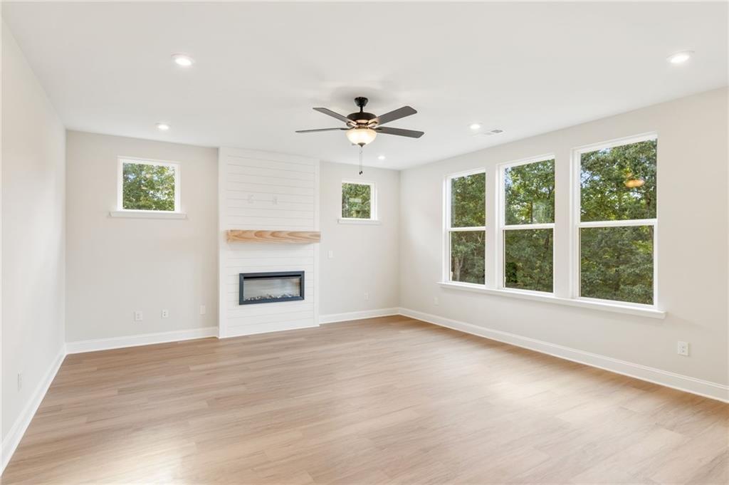 Spacious great room with shiplap gas fireplace, wooden mantel, ceiling fan, and tree-view windows in The Hickory B, Buford, GA