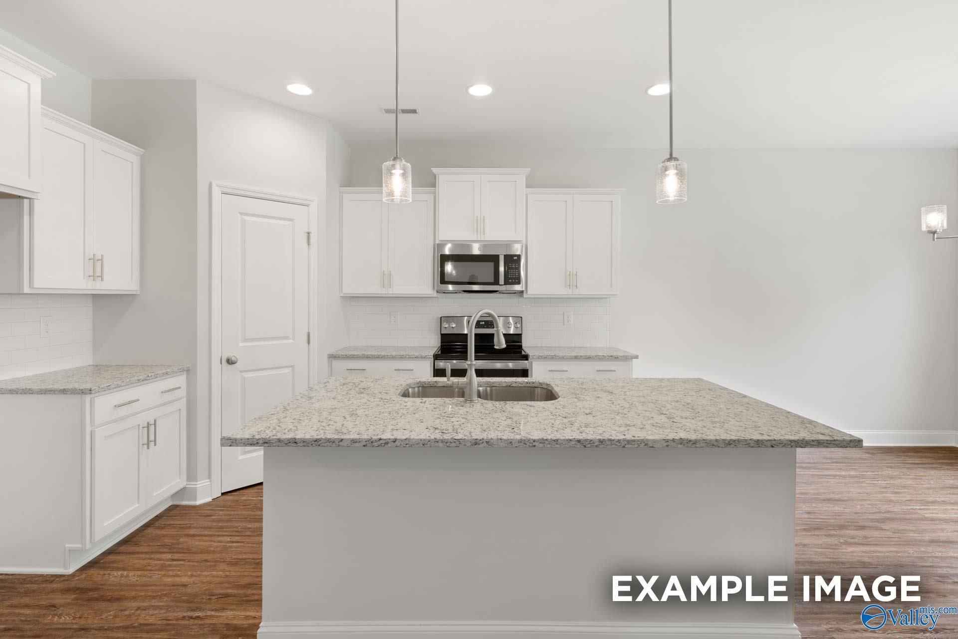 Modern white kitchen with granite island sink, stainless appliances, pendant lights in The Asheville C, Meridianville AL