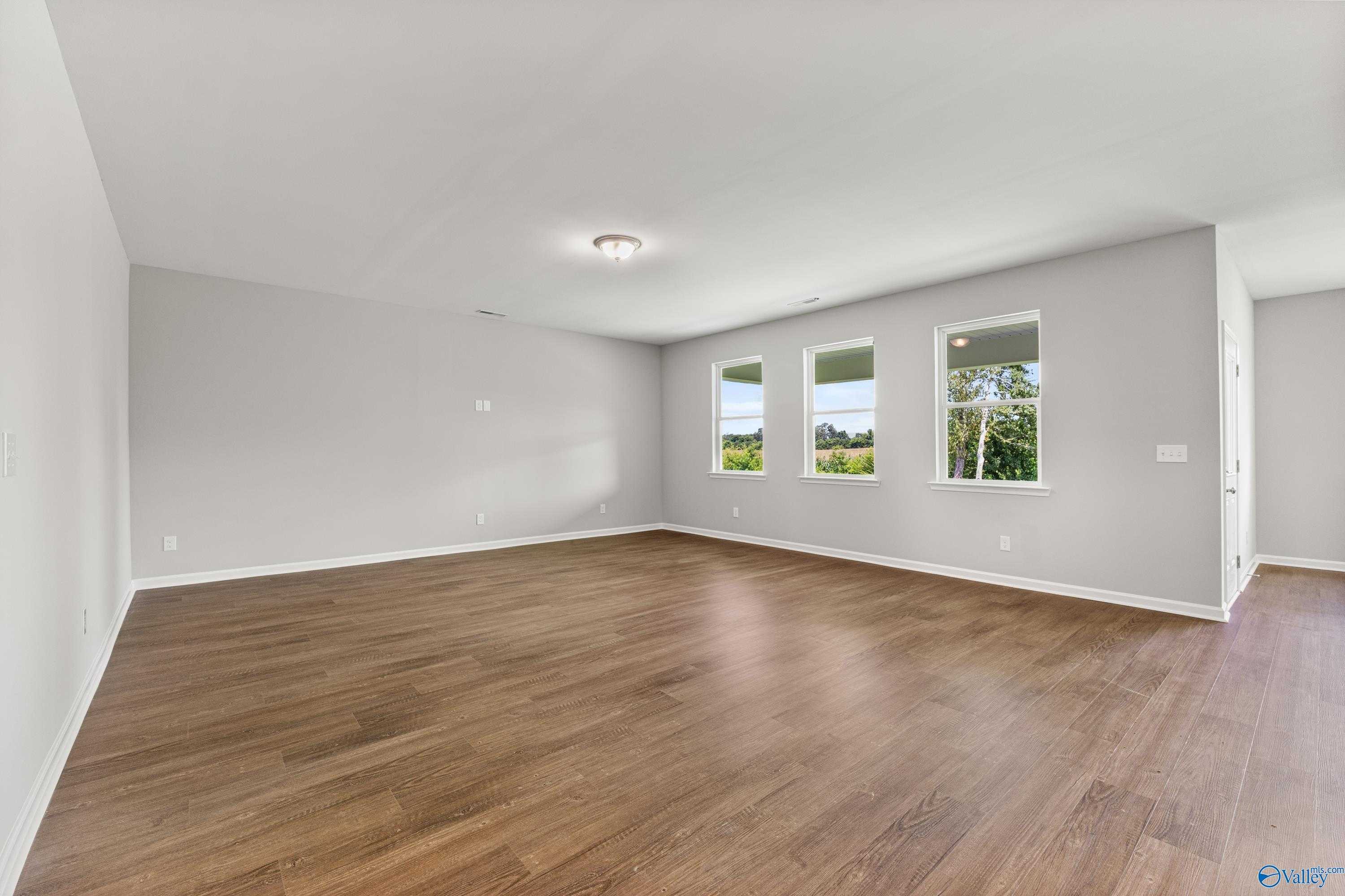 Spacious empty living room with hardwood floors, large windows, and gray walls in Davidson Homes The Sanctuary, Huntsville AL