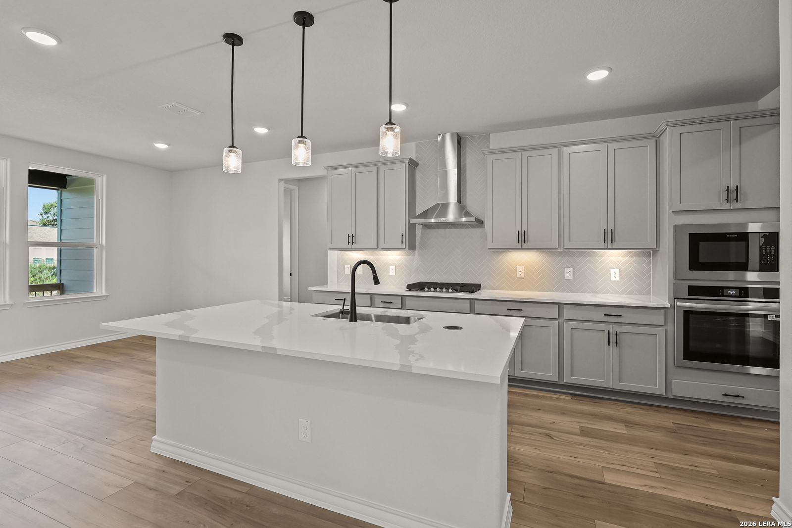 Modern kitchen with white quartz island, gray shaker cabinets, and stainless appliances in Davidson Homes Oxford F, Castroville TX