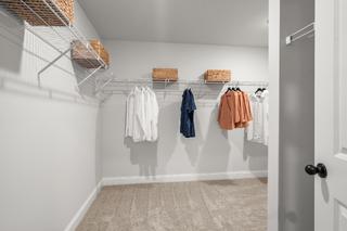 Spacious walk-in closet in The Washington H townhome with hanging clothes, wire shelves, and wicker baskets in Marietta GA