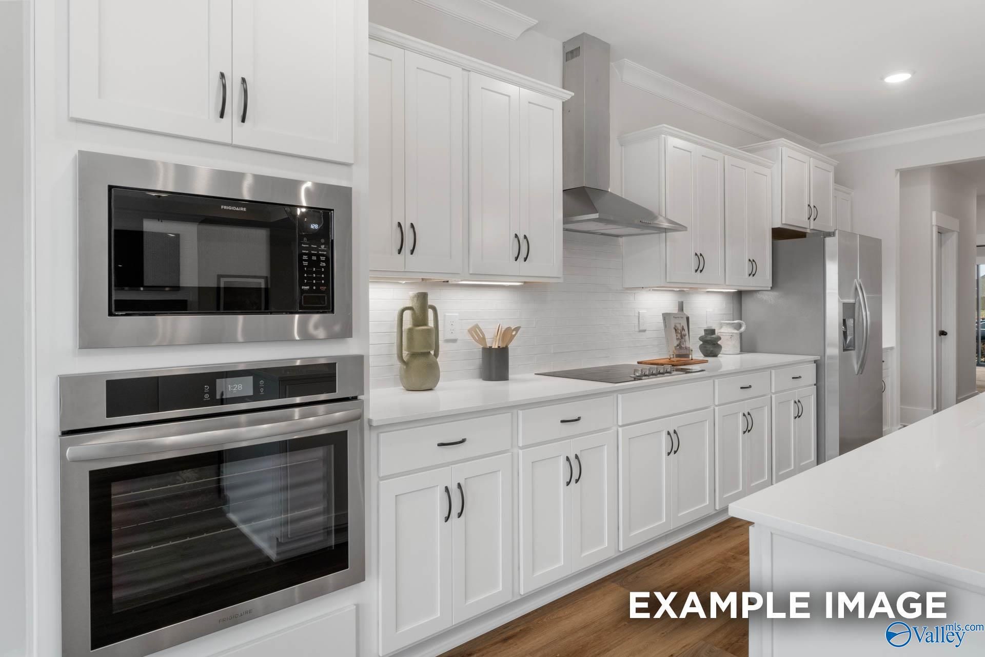 Modern white kitchen with stainless steel oven, microwave, island, and cabinets in The Finleigh 5-bedroom home, Decatur, Alabama