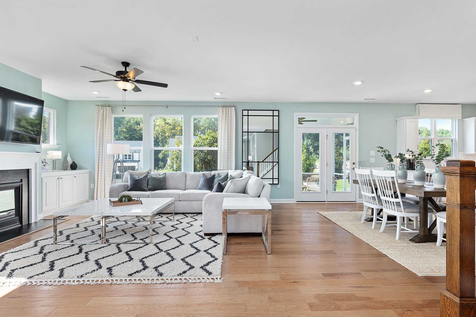 Spacious open-concept living dining room in Highland Forest Fuquay-Varina NC with gray sectional sofa hardwood floors fireplace and large windows