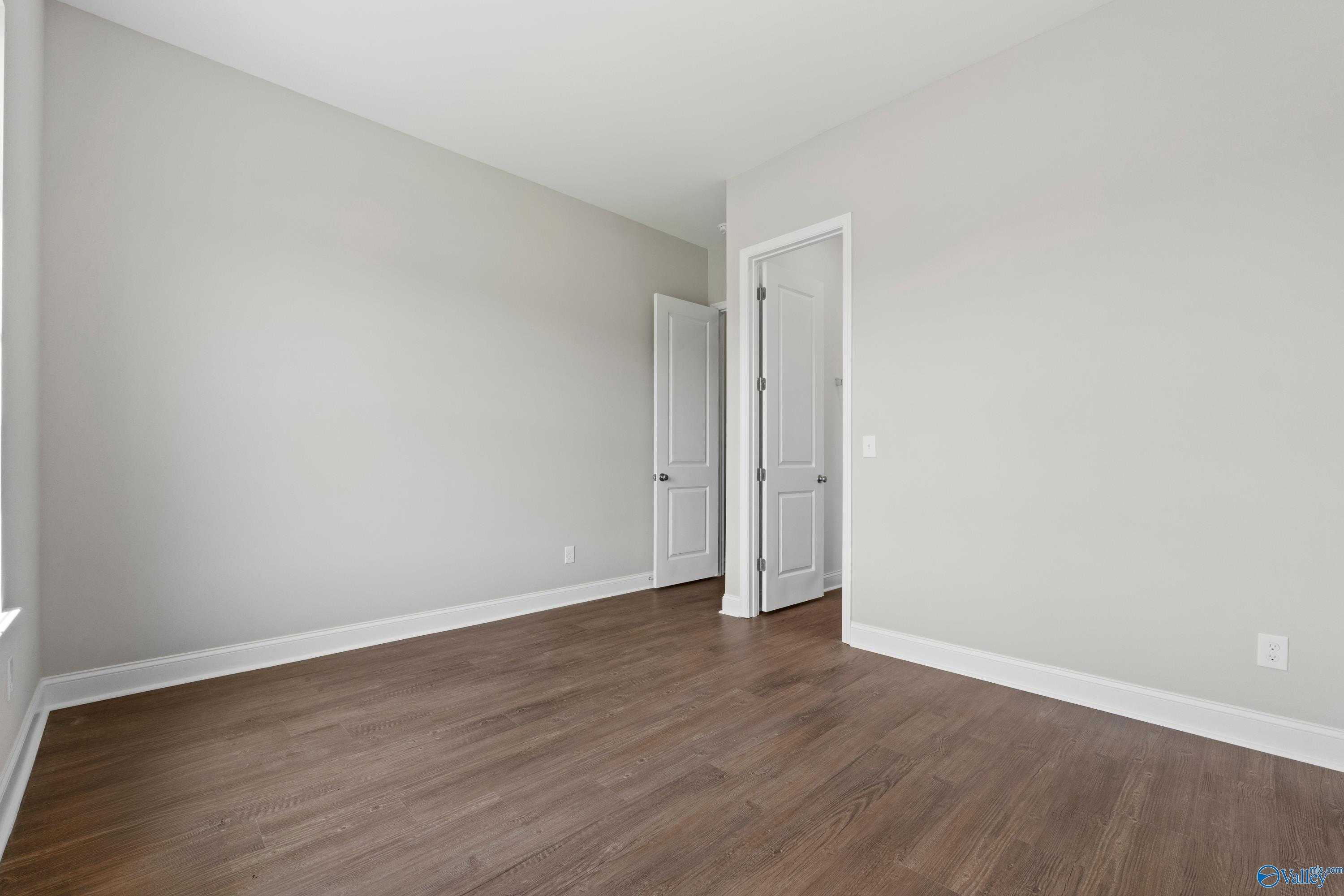 Spacious empty bedroom with light gray walls, hardwood floors, and adjacent doors in Davidson Homes The Arcadia, Huntsville