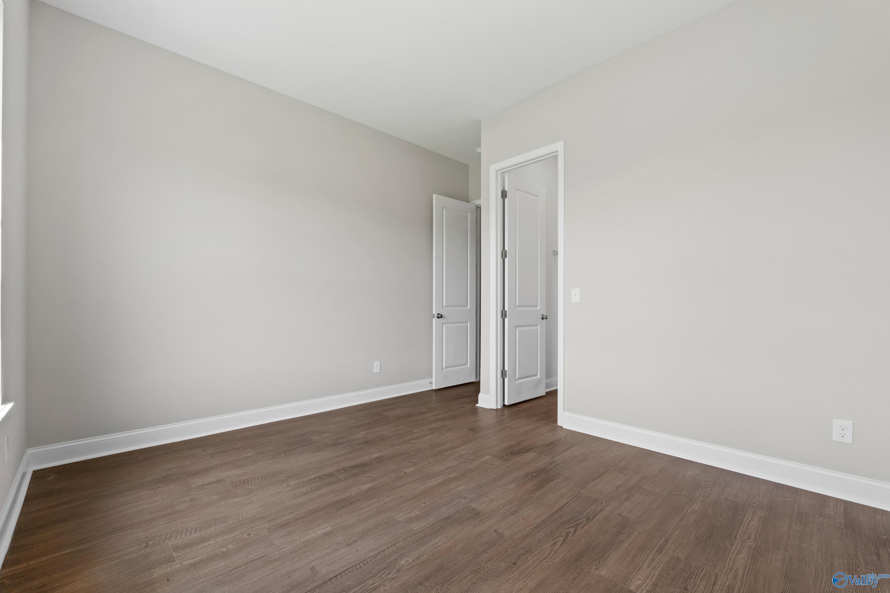 Spacious empty bedroom with light gray walls, hardwood floors, double doors to adjacent bath in Davidson Homes The Arcadia B, Huntsville
