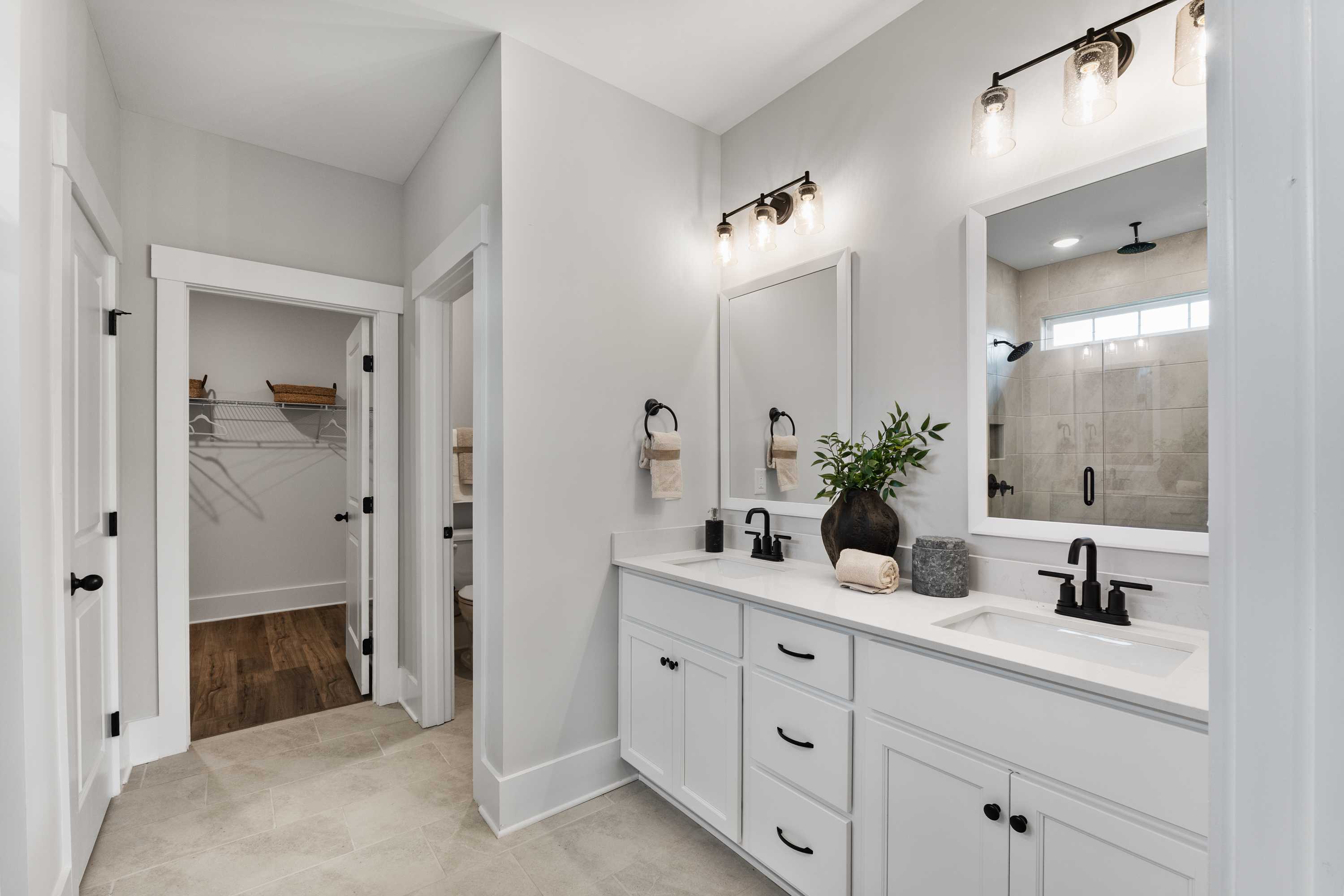 Primary bathroom at River Road Estates Decatur AL with double vanity white cabinets gray walls frameless glass shower walk-in closet