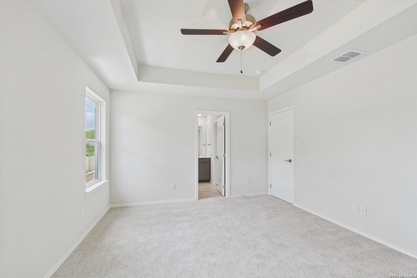 Bright primary bedroom with tray ceiling and en-suite bathroom in The Charlotte B floor plan at Meadows at Oak Creek.