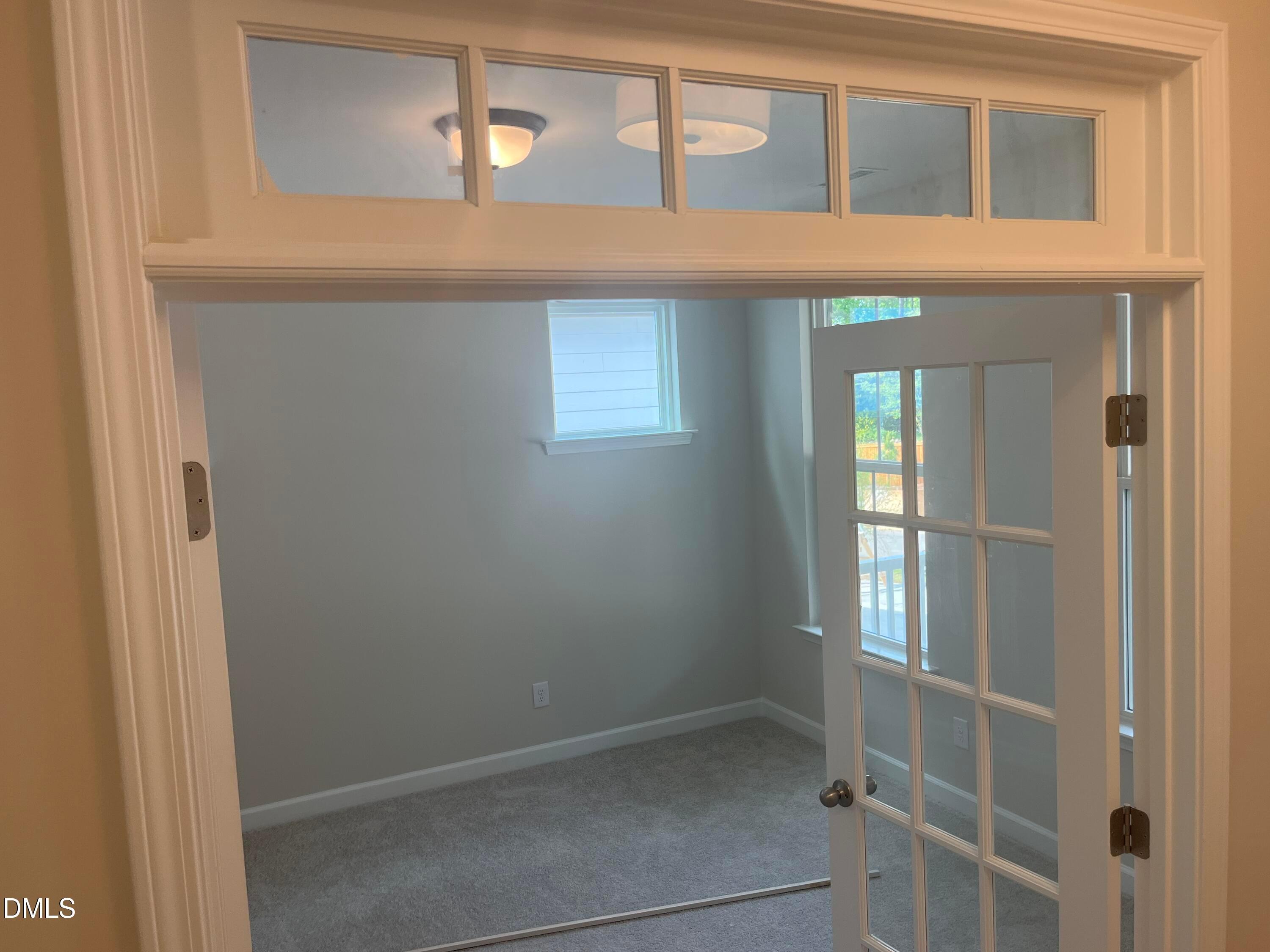 Bright study with transom windows, open French doors to backyard, light gray walls and carpet in Ashport L home, Wake Forest NC