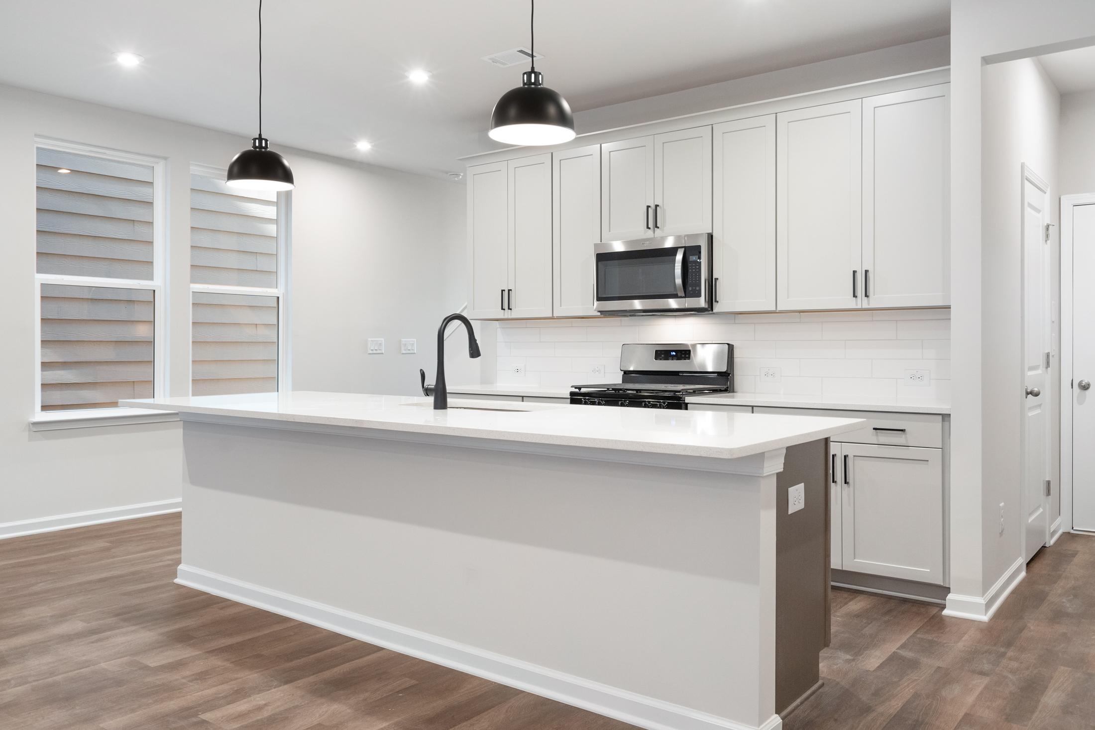 Spacious kitchen in The Cary B Davidson Homes plan featuring white shaker cabinets, large center island with farmhouse sink, and stainless steel appliances
