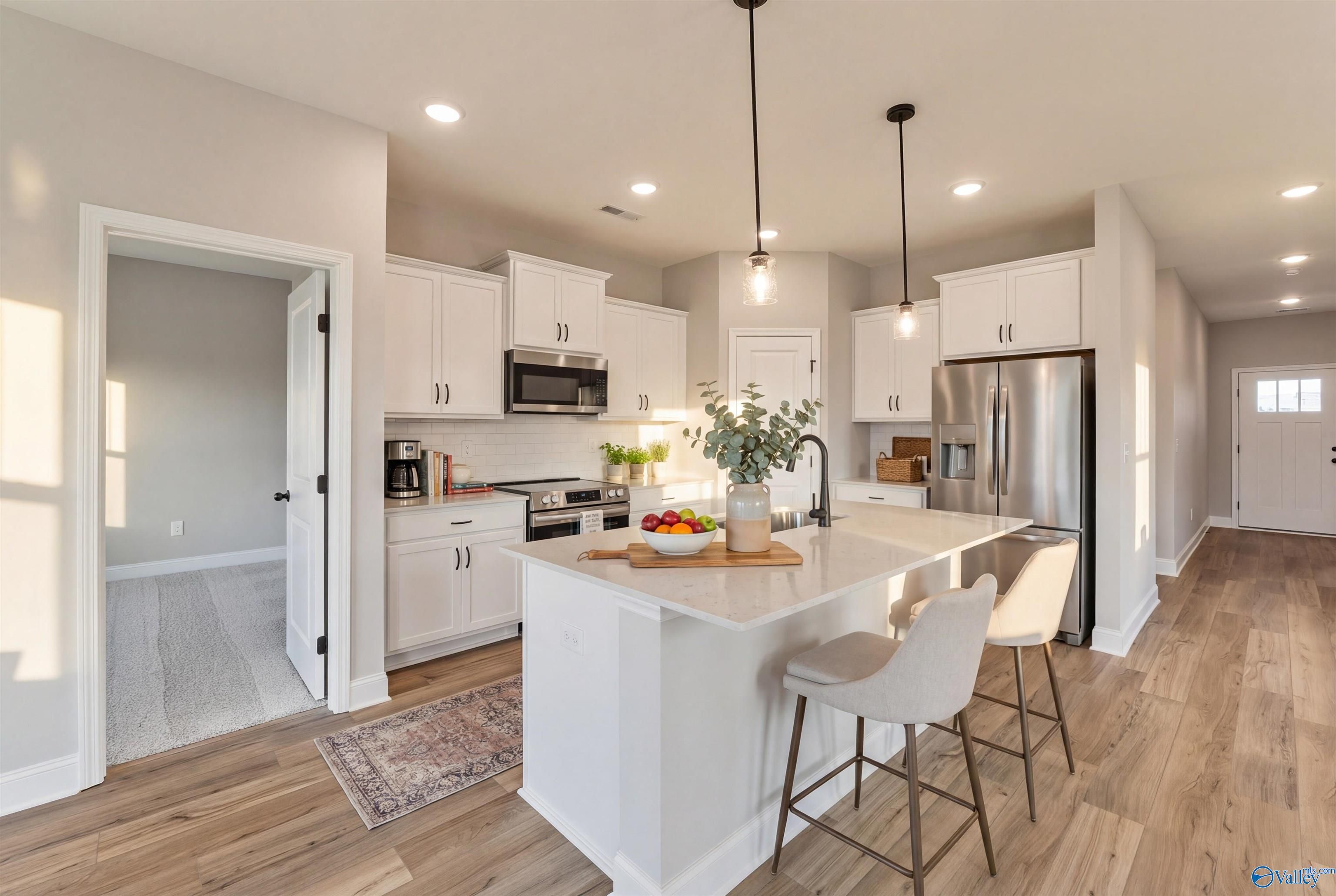 Modern white kitchen island with bar stools, stainless appliances, and pendant lights in Davidson Homes The Franklin B, Hazel Green, AL