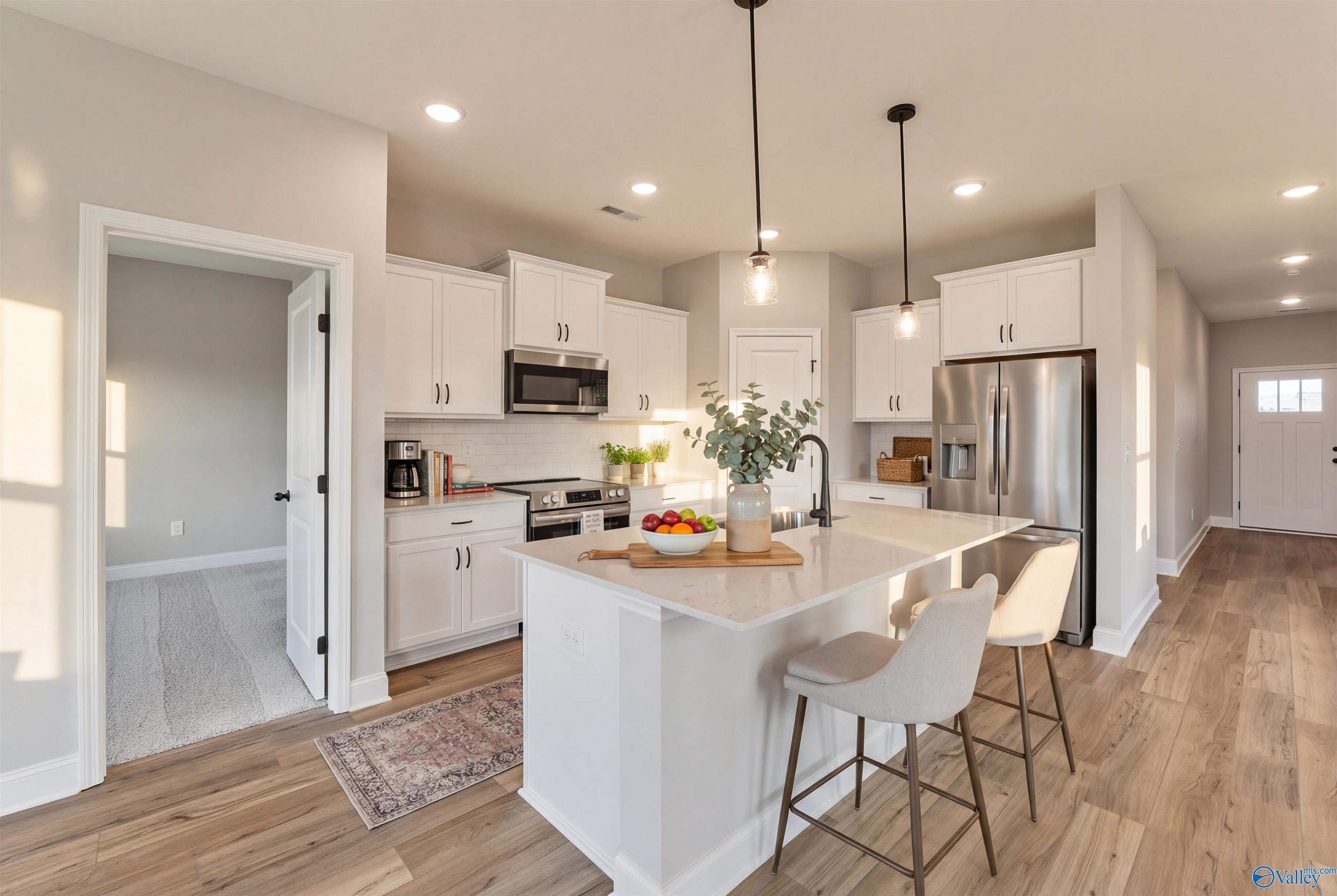 Modern white kitchen island with stainless appliances, pendant lights, and open layout in Davidson Homes The Franklin B, Hazel Green, Alabama