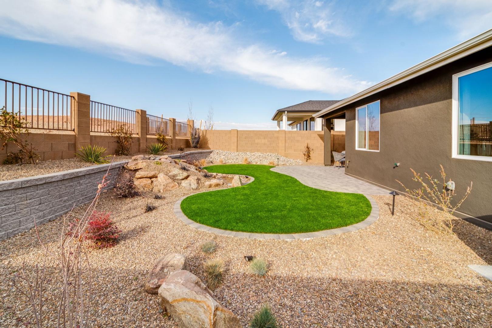 Landscaped backyard of The Newport home with circular turf, rock garden, gravel paths, stucco walls, and desert plants in Prescott AZ