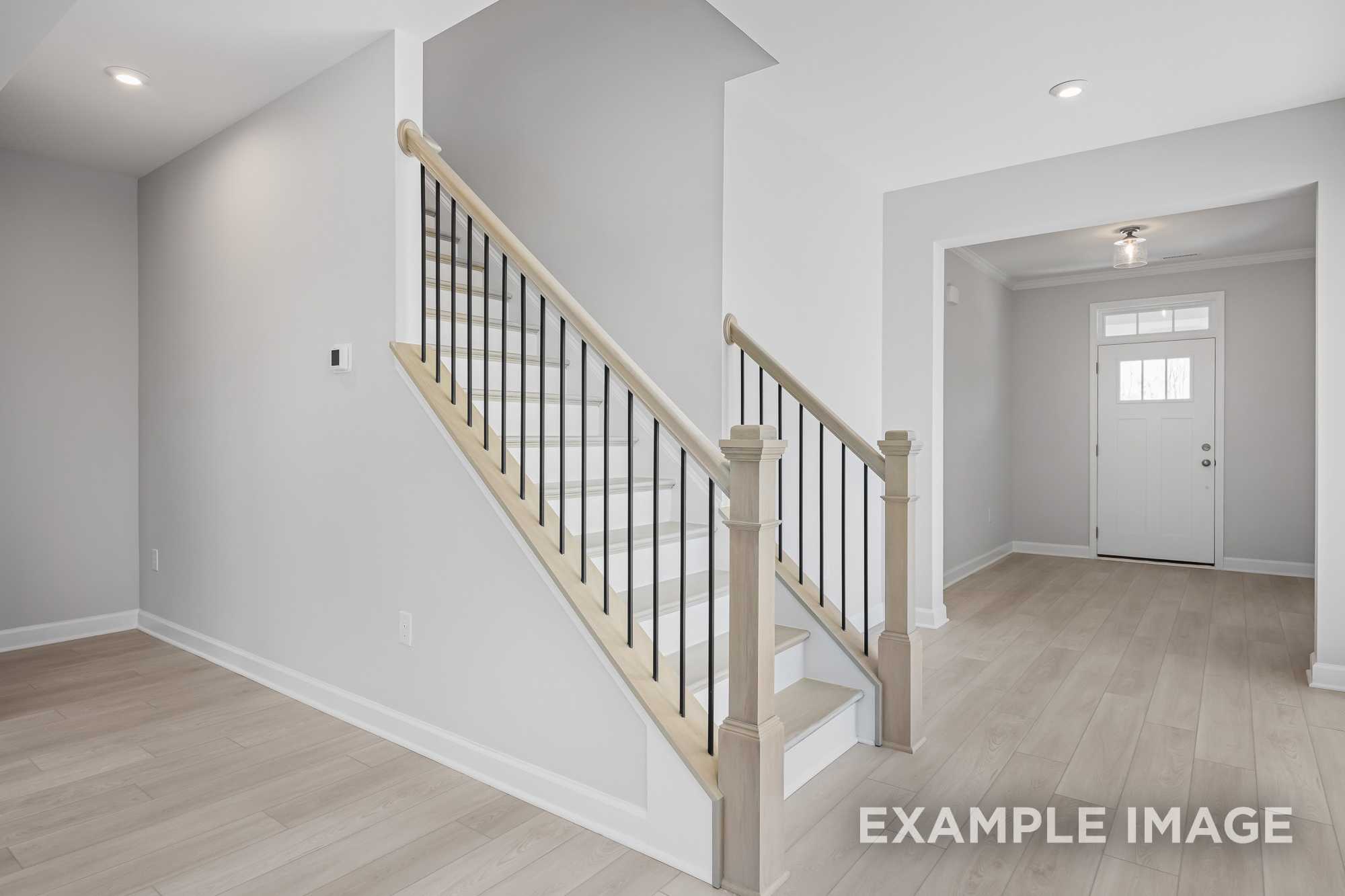 Spacious oak staircase with black metal balusters in The Cypress D II two-story home, open entryway and hardwood floors
