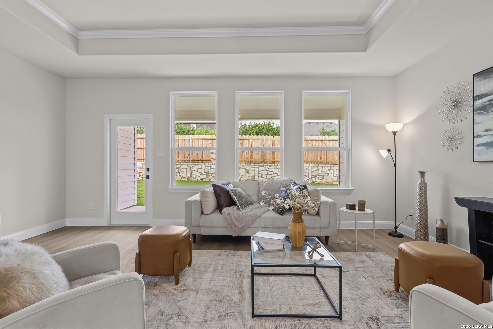 Bright living room with large windows overlooking backyard, beige sofa, glass coffee table in Davidson Homes The Lanier G, Castroville, Texas
