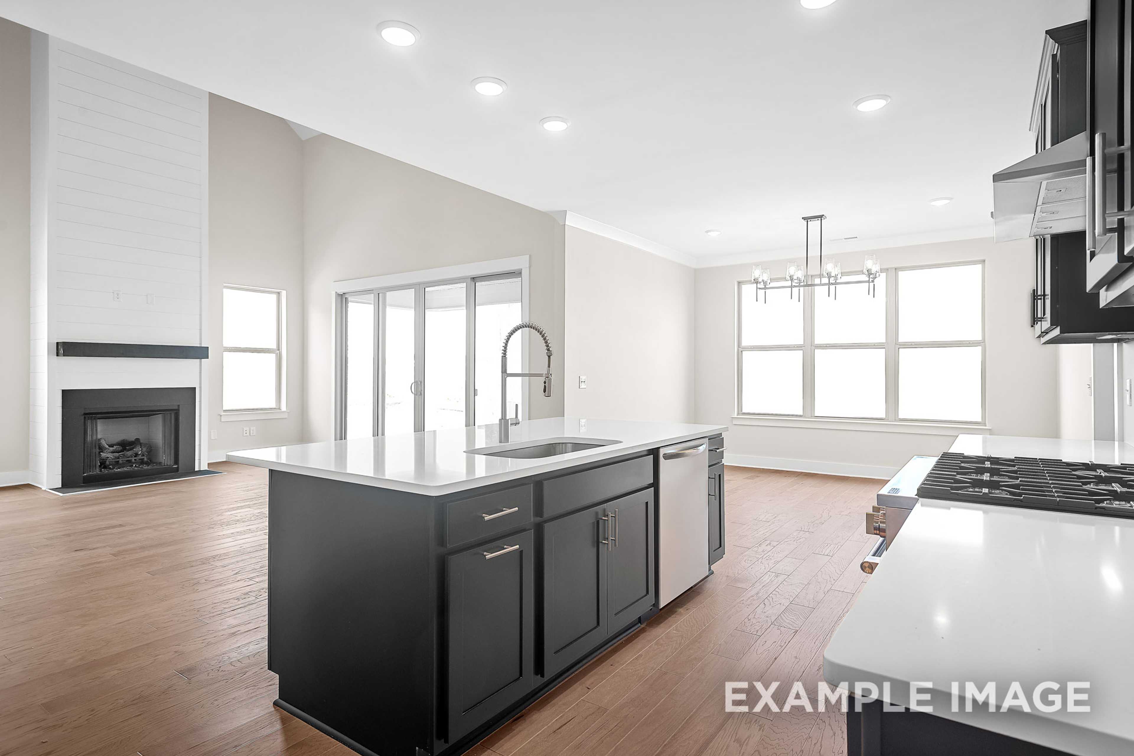 Spacious open-concept kitchen in The Hawkins home with black island, farmhouse sink, shiplap fireplace, and large windows