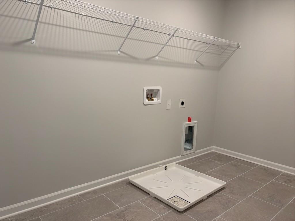 Spacious laundry room with wire shelving, washer-dryer hookups, pet door, and tiled floor in Davidson Homes Hickory B, Winder, Georgia