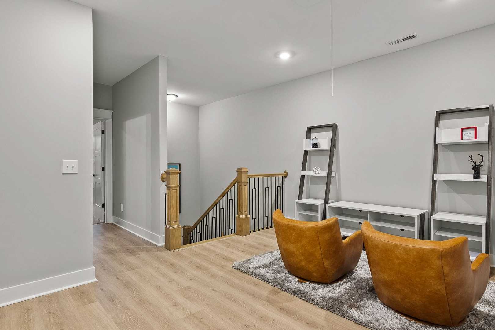Cozy upper-level loft in The Oxford home design featuring leather armchairs, white shelving, oak staircase, and light wood floors