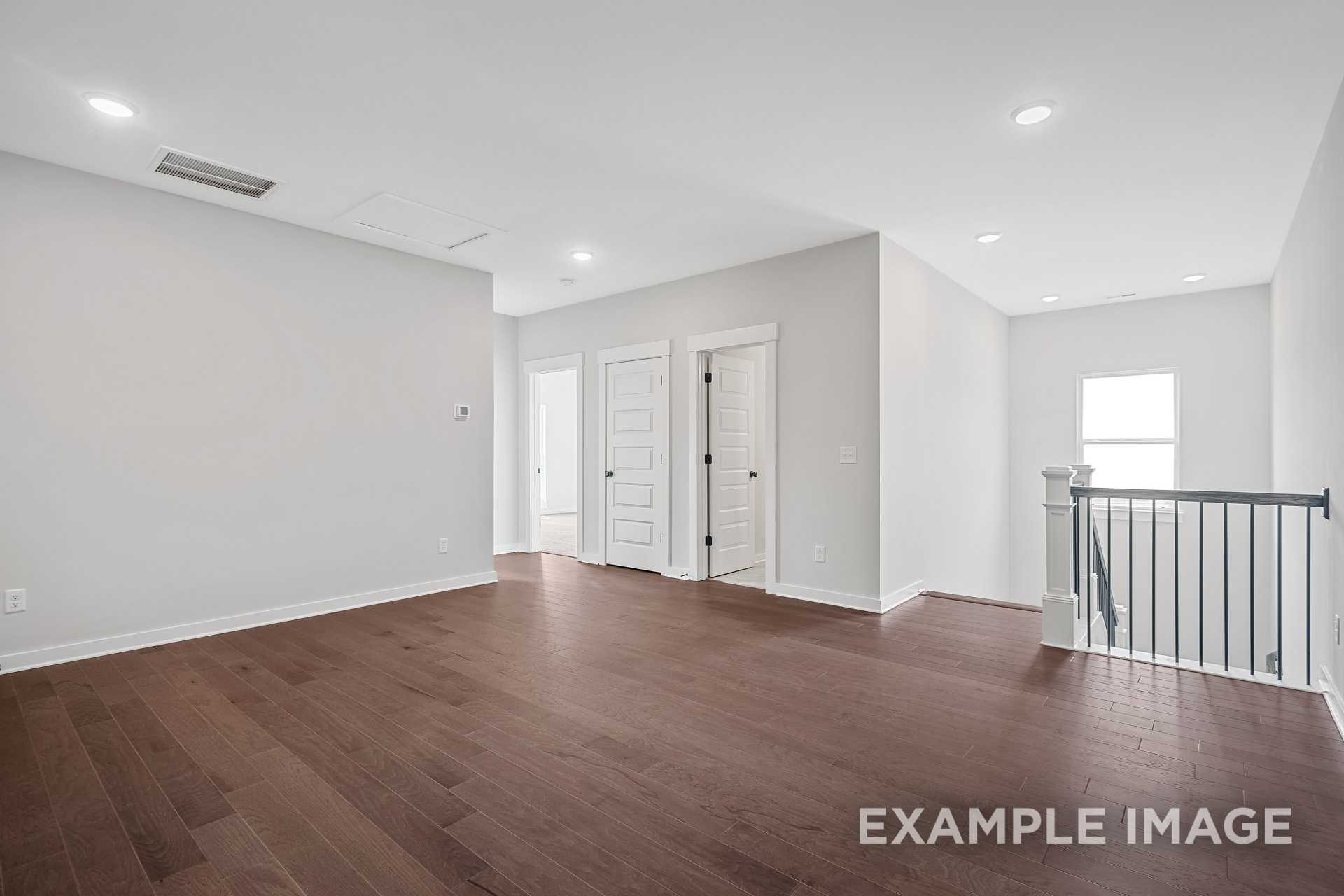 Spacious upstairs hallway in The Hathaway 2-story home featuring hardwood floors, white bedroom doors, and open railing overlook