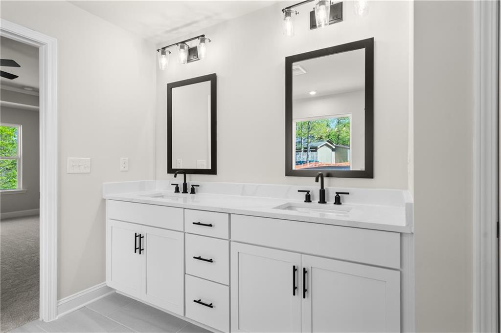 Elegant double vanity bathroom with white shaker cabinets, black faucets, quartz counters, and mirrors in Davidson Homes The Hickory E, Buford, GA