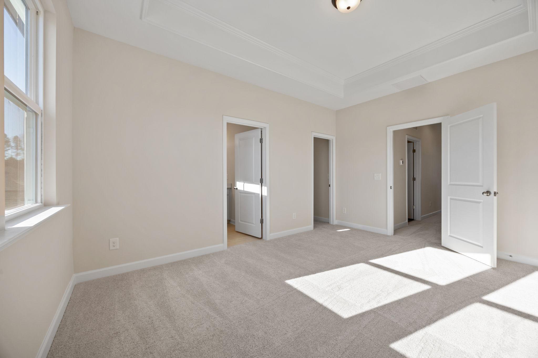 Spacious bedroom with tray ceiling and carpeted flooring at Forestville Yard in Knightdale by Davidson Homes