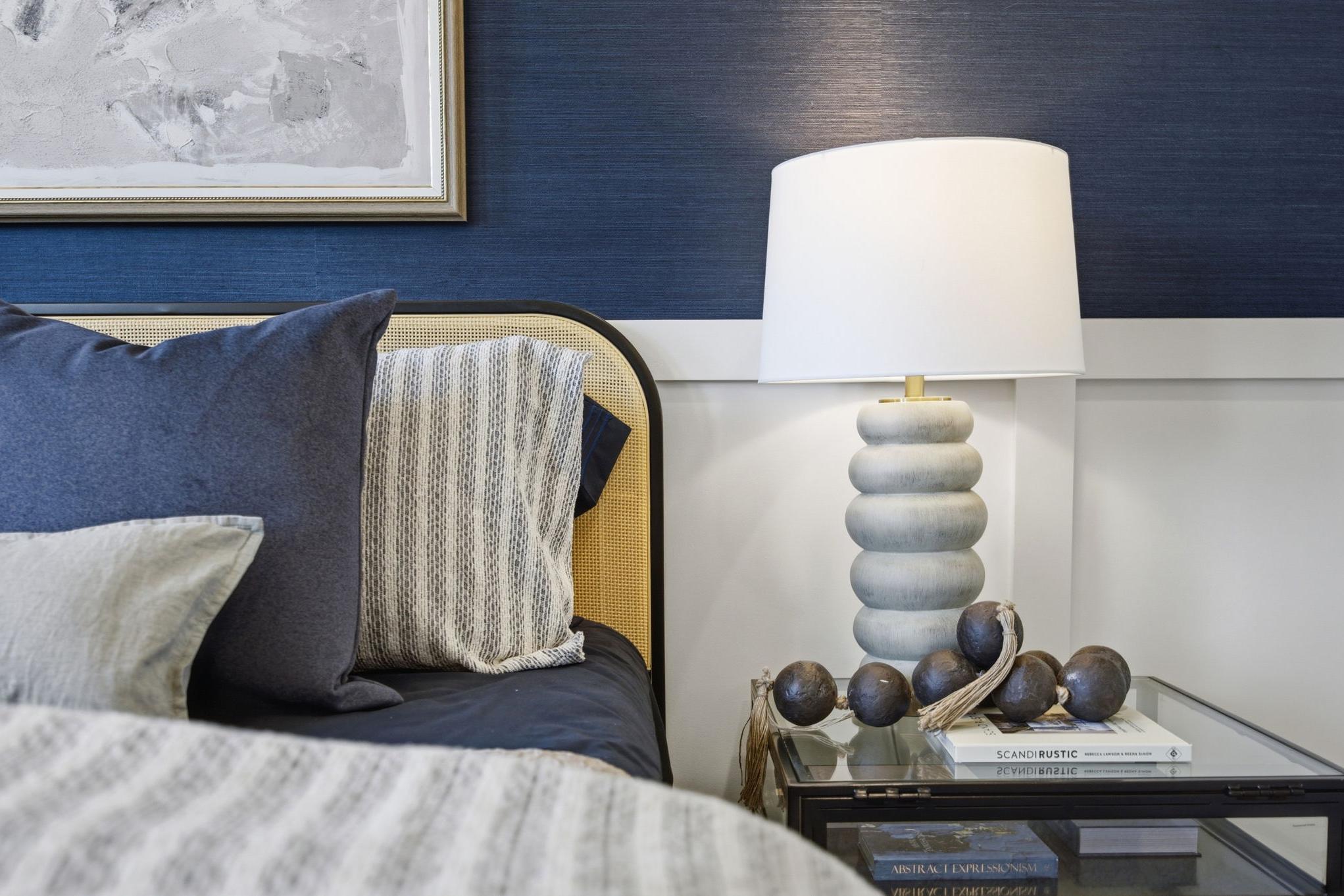 Master suite bedroom in The Burke C featuring a caned headboard, navy blue accent wall, and modern nightstand decor.