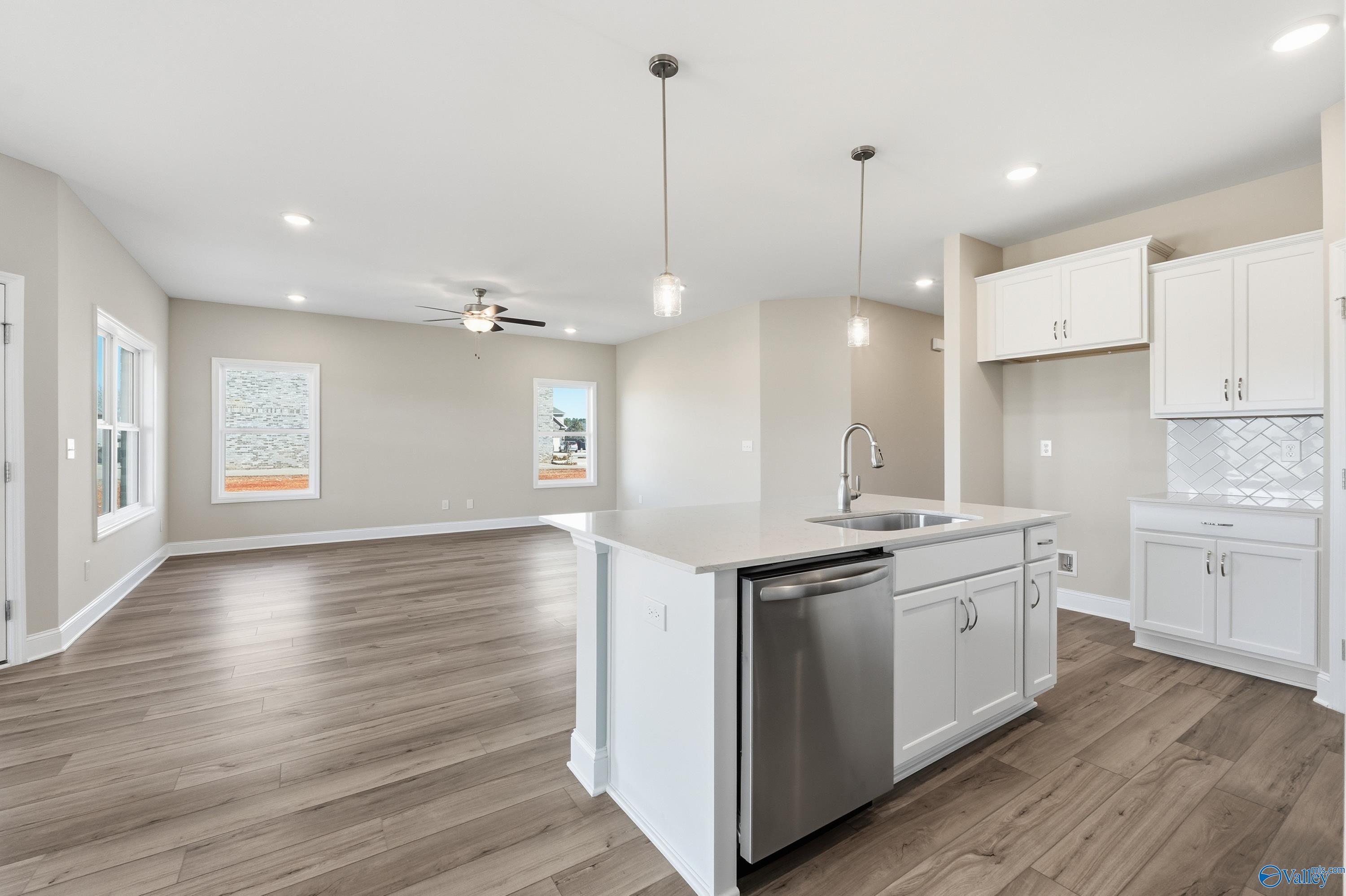 Modern open kitchen with white shaker cabinets, stainless steel appliances, island sink, and hardwood floors in Davidson Homes The Franklin C, New Market, Alabama