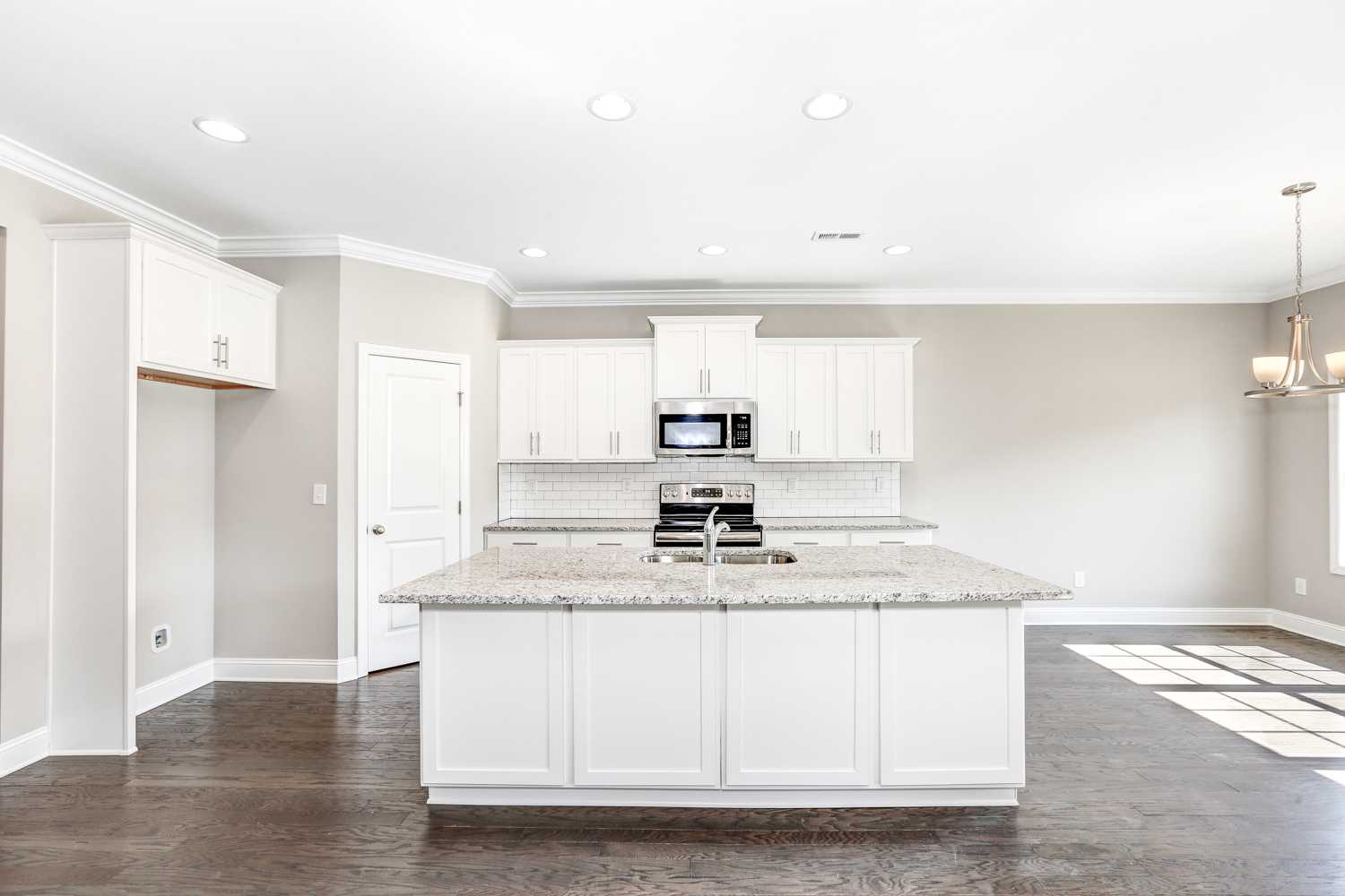 Spacious The Montgomery kitchen with white shaker cabinets, granite island sink, stainless appliances, subway tile, hardwood floors