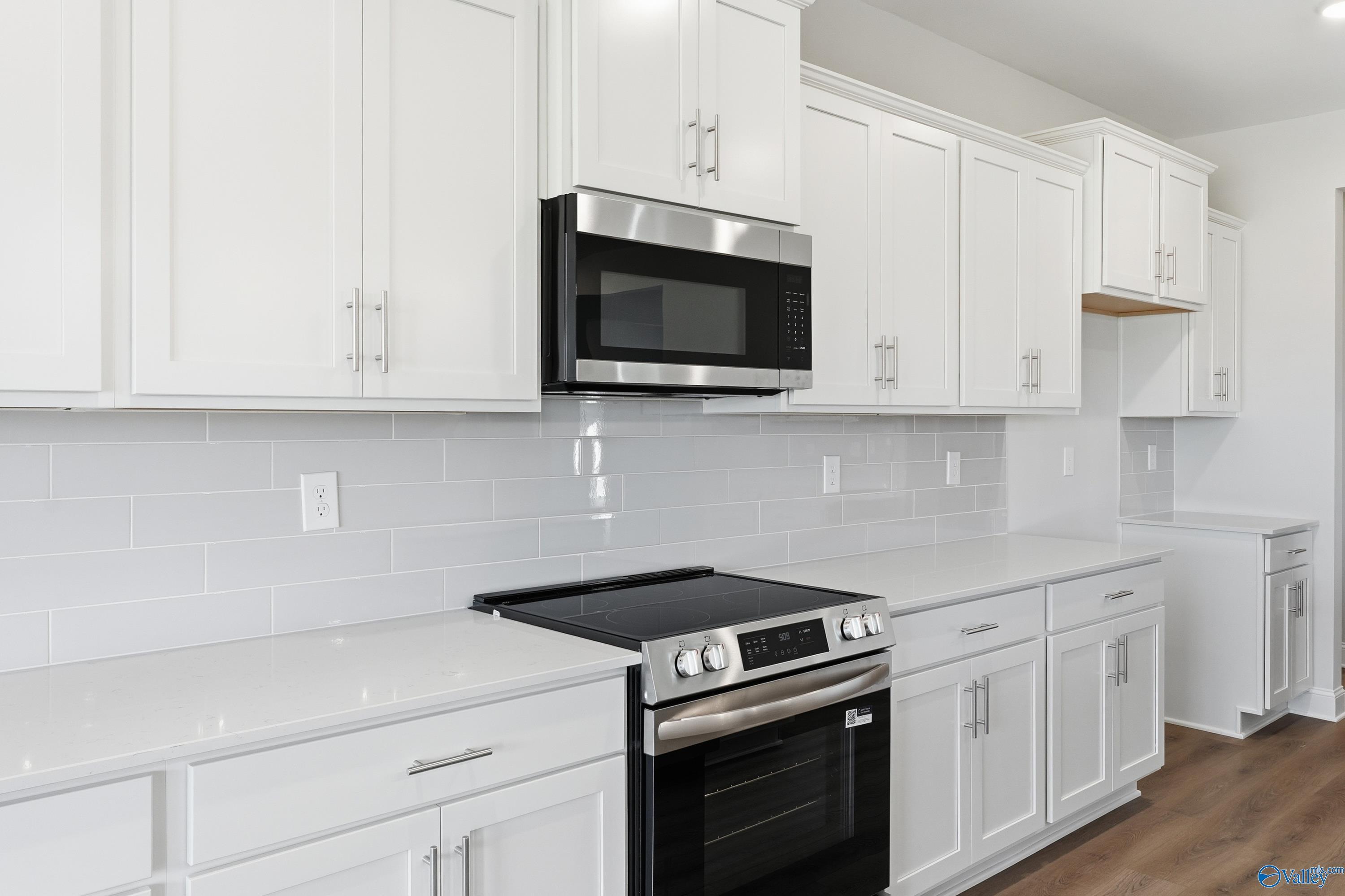 Modern white kitchen with stainless steel microwave, oven, and subway tile backsplash in Davidson Homes The Finleigh, Harvest, AL