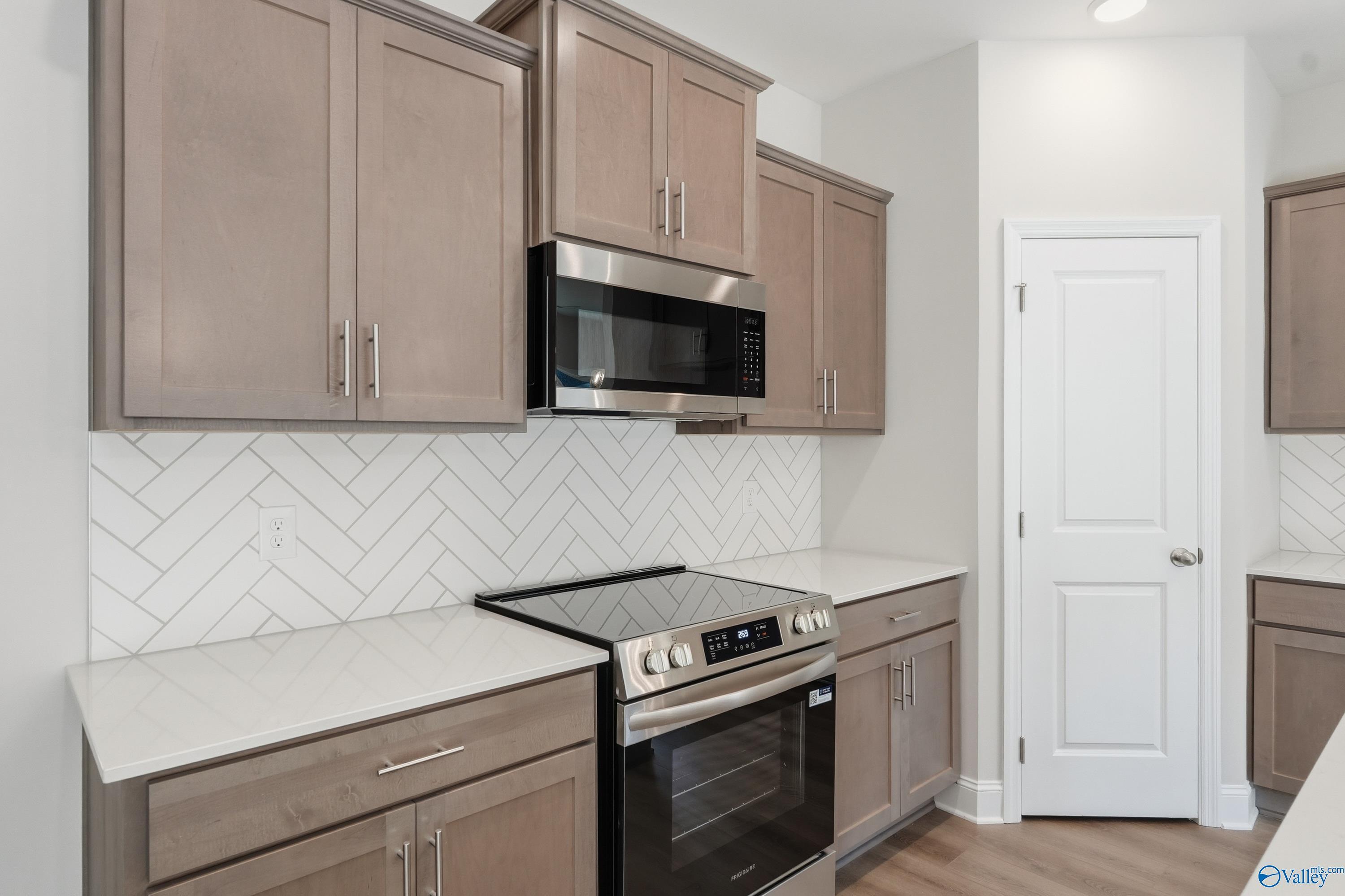 Modern kitchen featuring beige shaker cabinets, stainless steel oven and microwave, quartz counters, herringbone tile backsplash in The Daphne C, Arab, AL