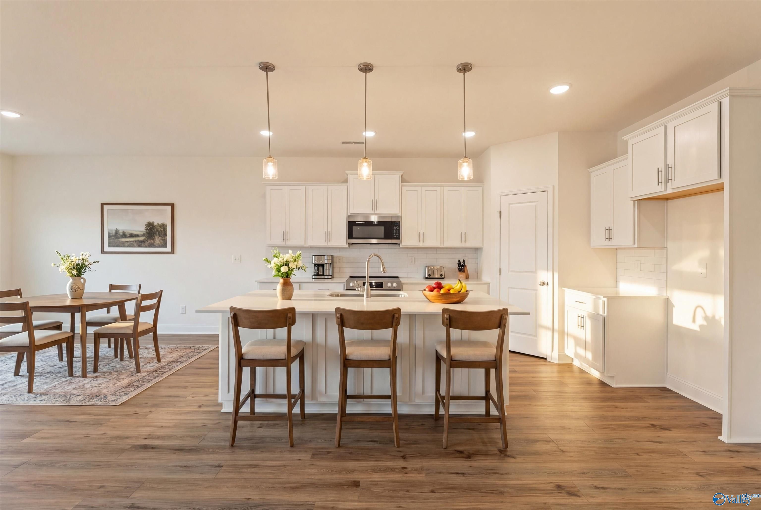 Modern open-concept kitchen with white cabinets, granite island, stainless appliances, and hardwood floors in Davidson Homes The Rockford B, Toney, Alabama