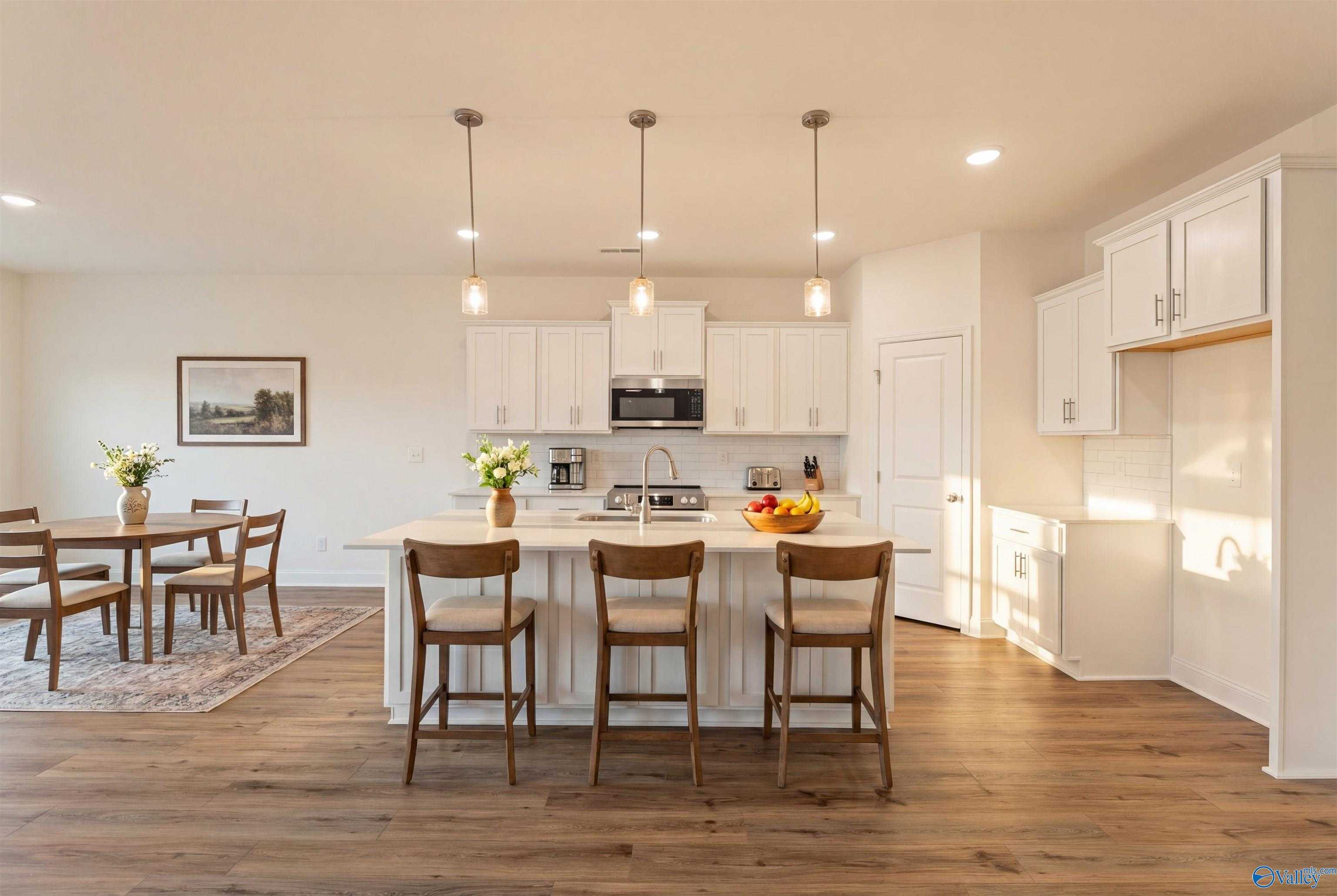 Modern open-concept kitchen with white cabinets, granite island, stainless appliances, and hardwood floors in Davidson Homes The Rockford B, Toney, Alabama