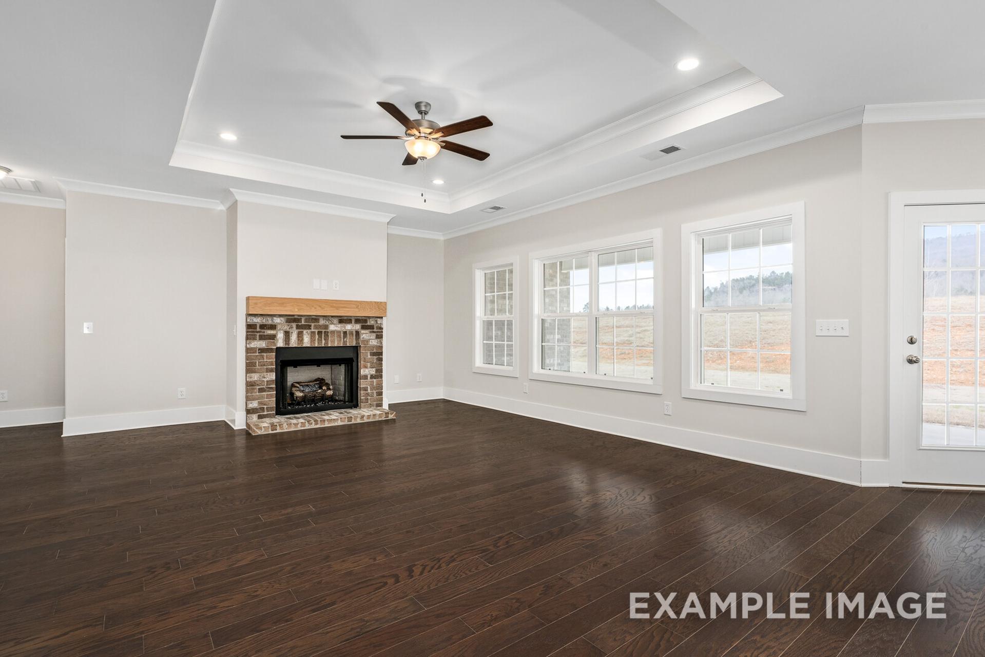 Spacious great room in The Rockford home with brick fireplace, large windows, ceiling fan, and hardwood floors