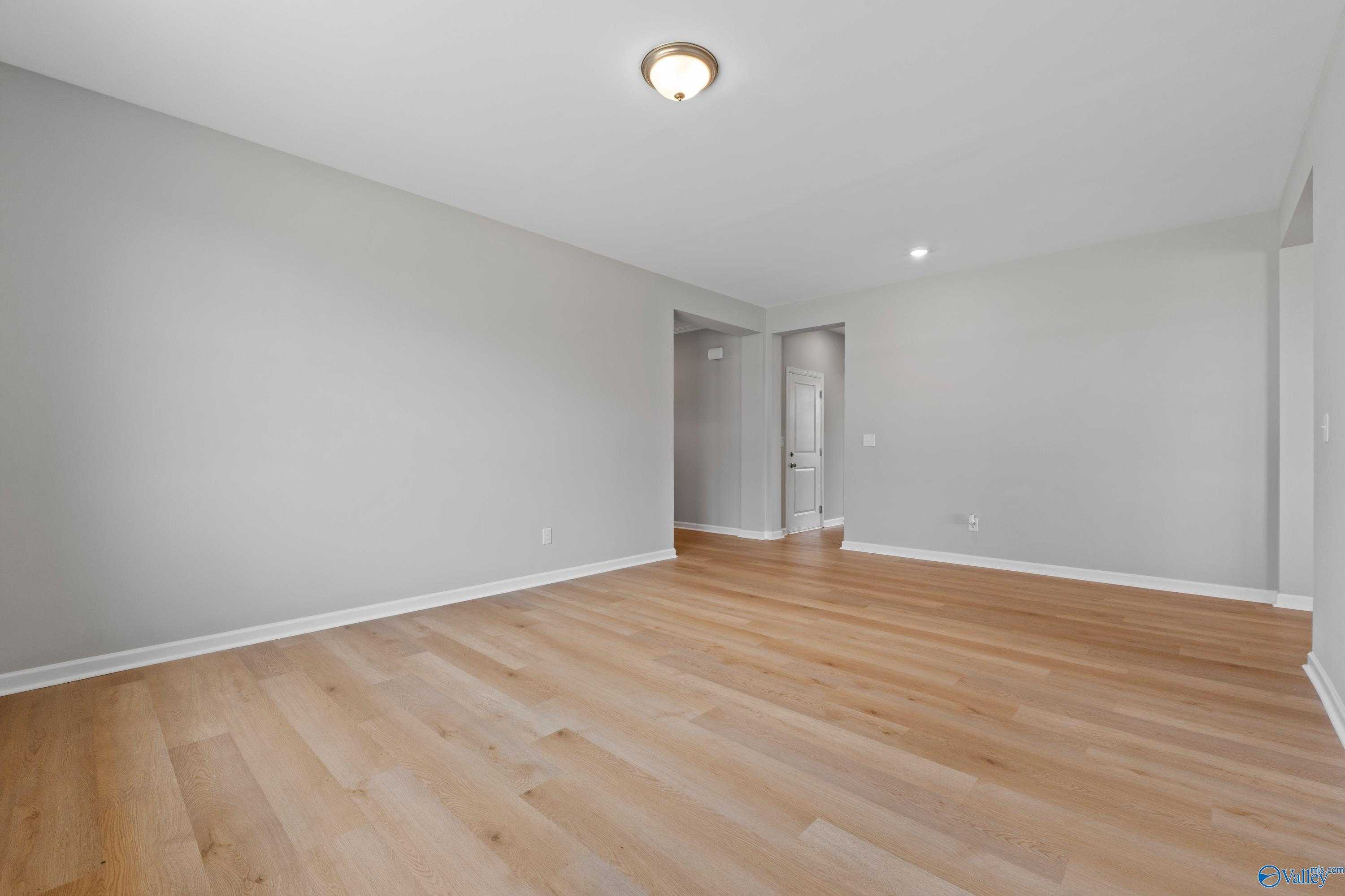 Spacious empty living room with light gray walls, oak hardwood floors, and open archways in Davidson Homes The Orion, Athens AL