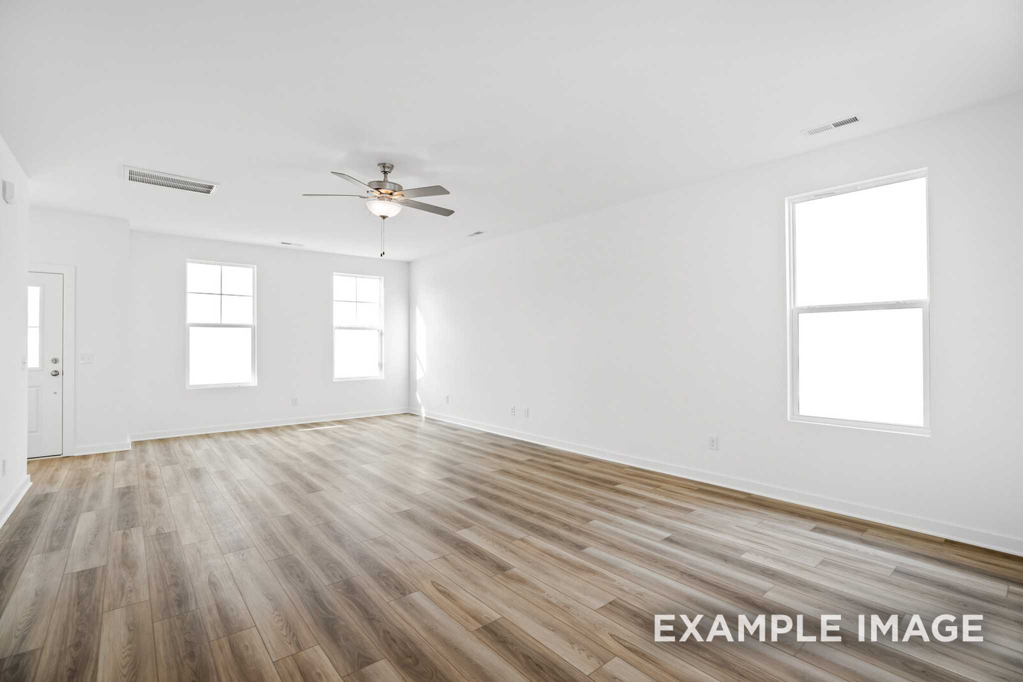 Spacious empty great room in The Murray B with hardwood floors, large windows, and ceiling fan