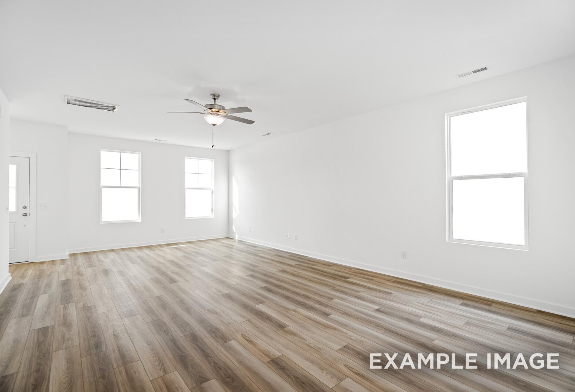 Spacious empty great room in The Murray B with hardwood floors, large windows, and ceiling fan