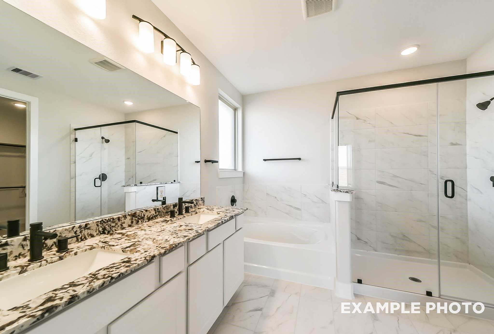 Elegant master bathroom featuring double marble vanity, freestanding tub, and frameless glass shower in Davidson Homes The Philip C, Rosharon, Texas