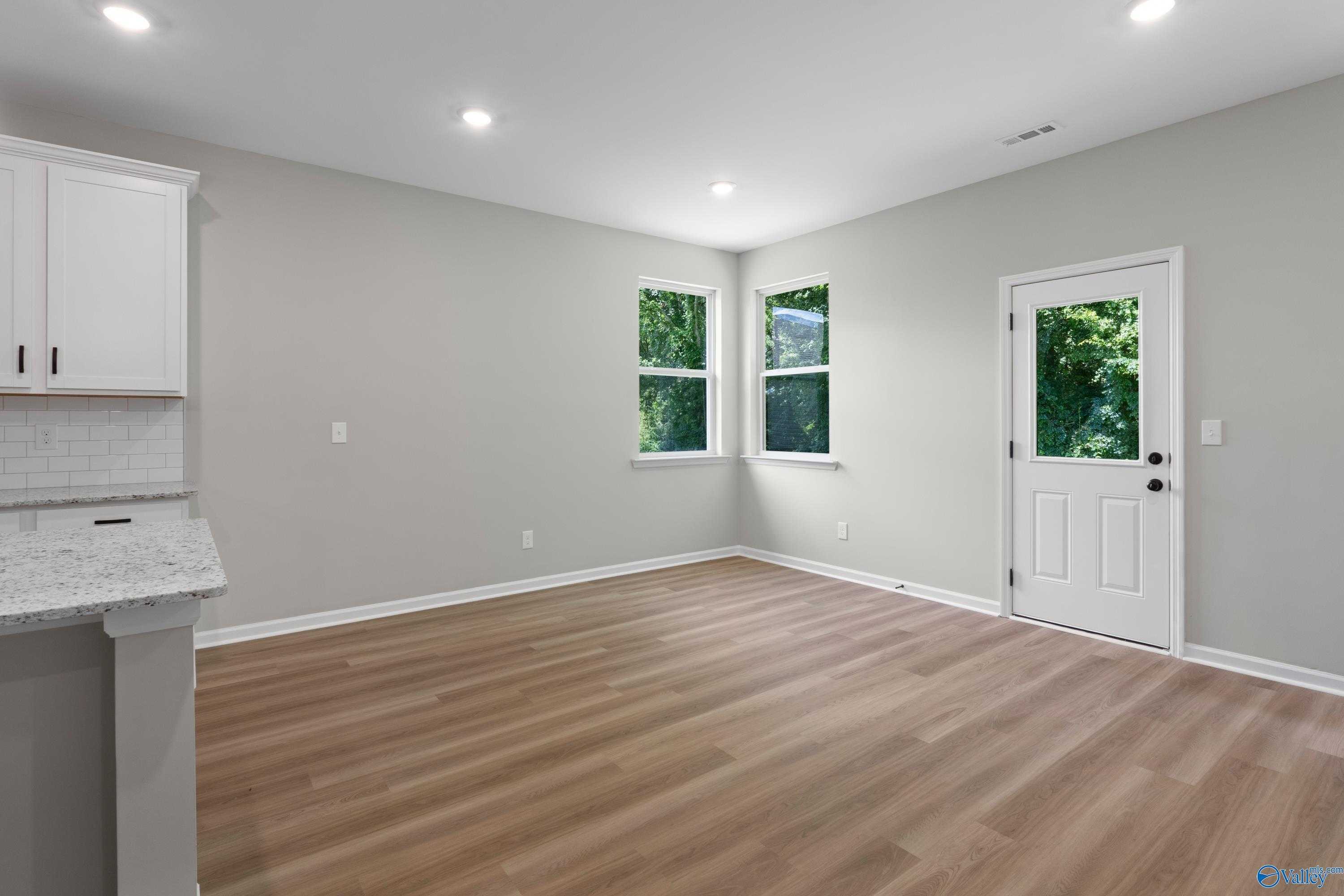 Bright modern kitchen with white cabinets, quartz counters, hardwood floors, and large green-view windows in The Phoenix home
