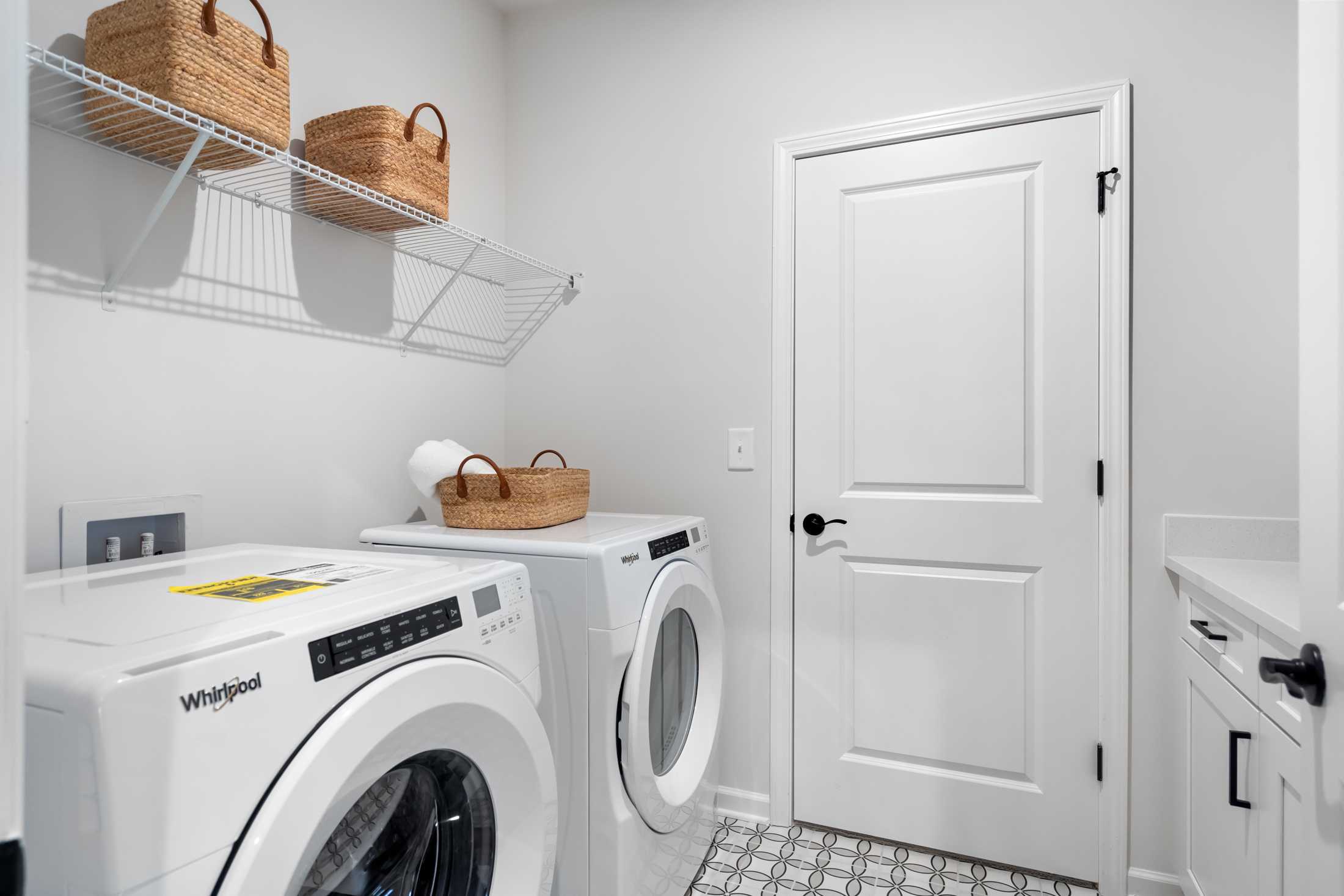 Modern laundry room in The Edison C by Davidson Homes featuring Whirlpool washer dryer and wicker basket shelves