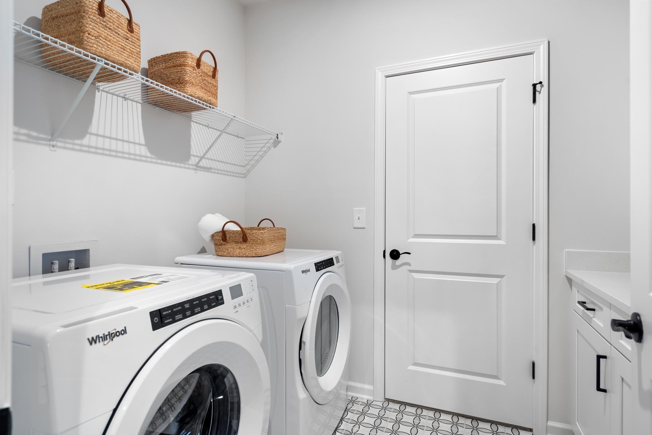 Modern laundry room in The Edison A Davidson Homes plan featuring Whirlpool washer dryer, wire shelves with wicker baskets, utility sink