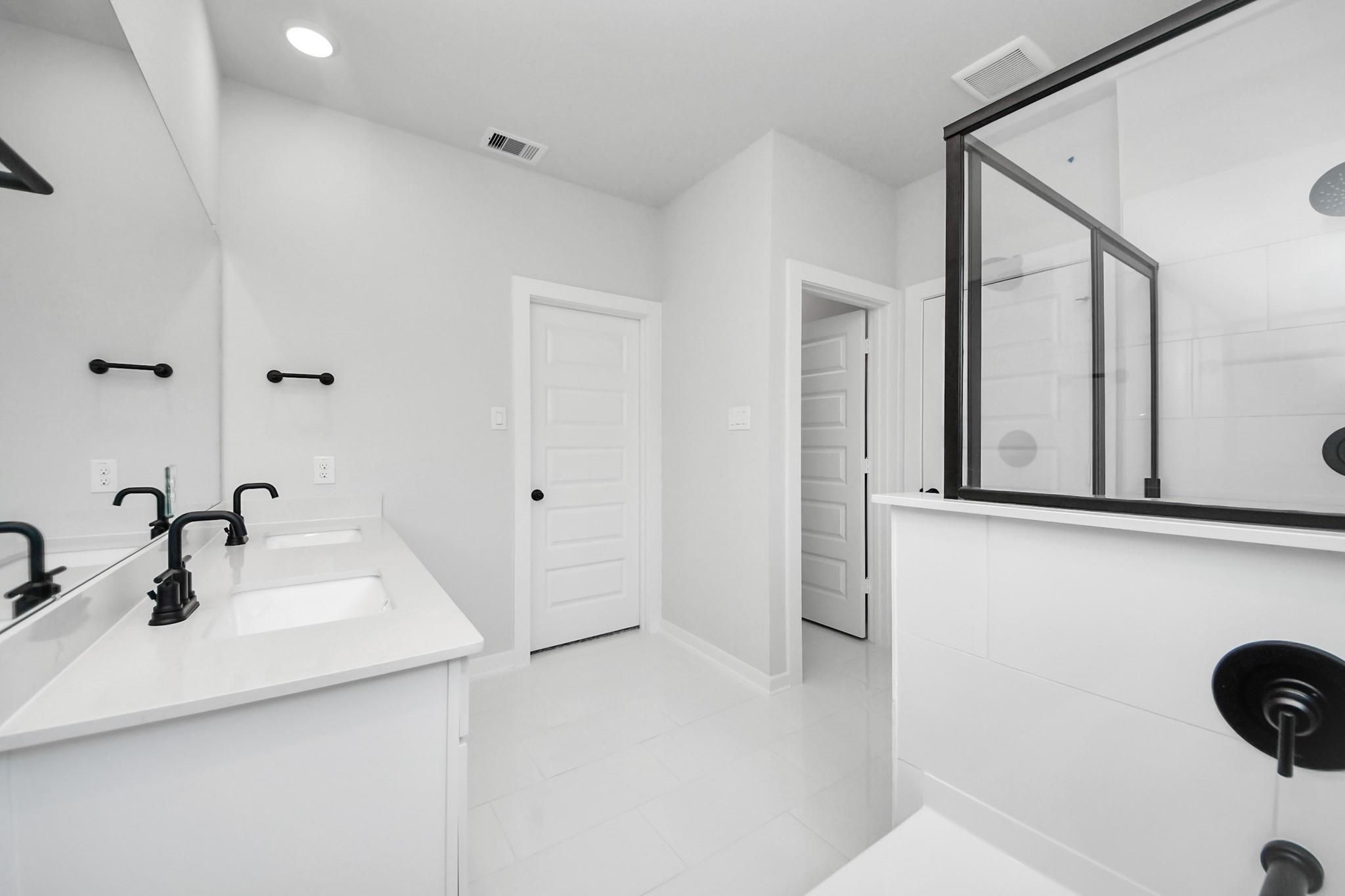 Modern primary bathroom with dual vanity, black fixtures, and walk-in shower in The Riviera C home, River Ranch Meadows.
