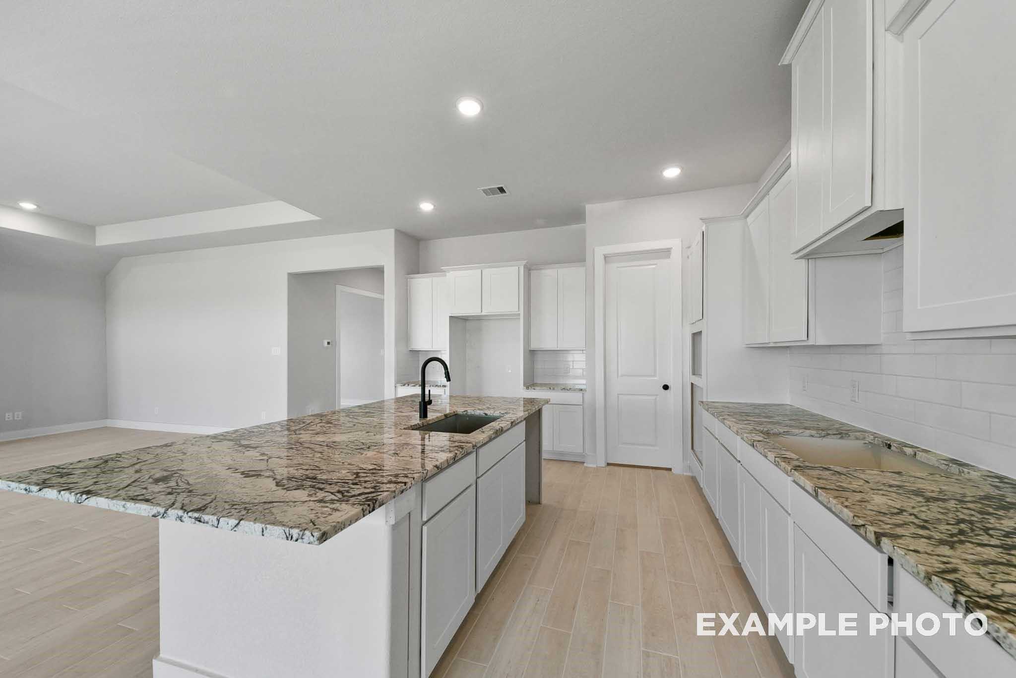 Open-concept kitchen with white shaker cabinets, veined granite island, subway tile backsplash in Davidson Homes The George A, Lago Mar Texas