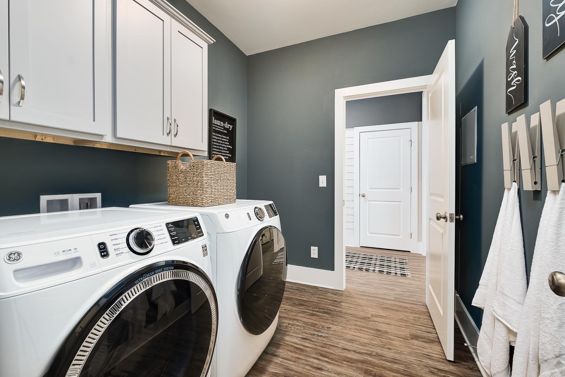 Spacious laundry room in The Everett Davidson Homes design with white washer dryer, cabinets, gray walls