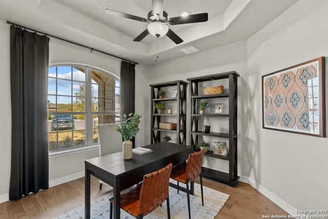 Elegant home office with black desk, leather chairs, bookshelves, plants, and arched window overlooking yard in The Summerlin B, Castroville, Texas