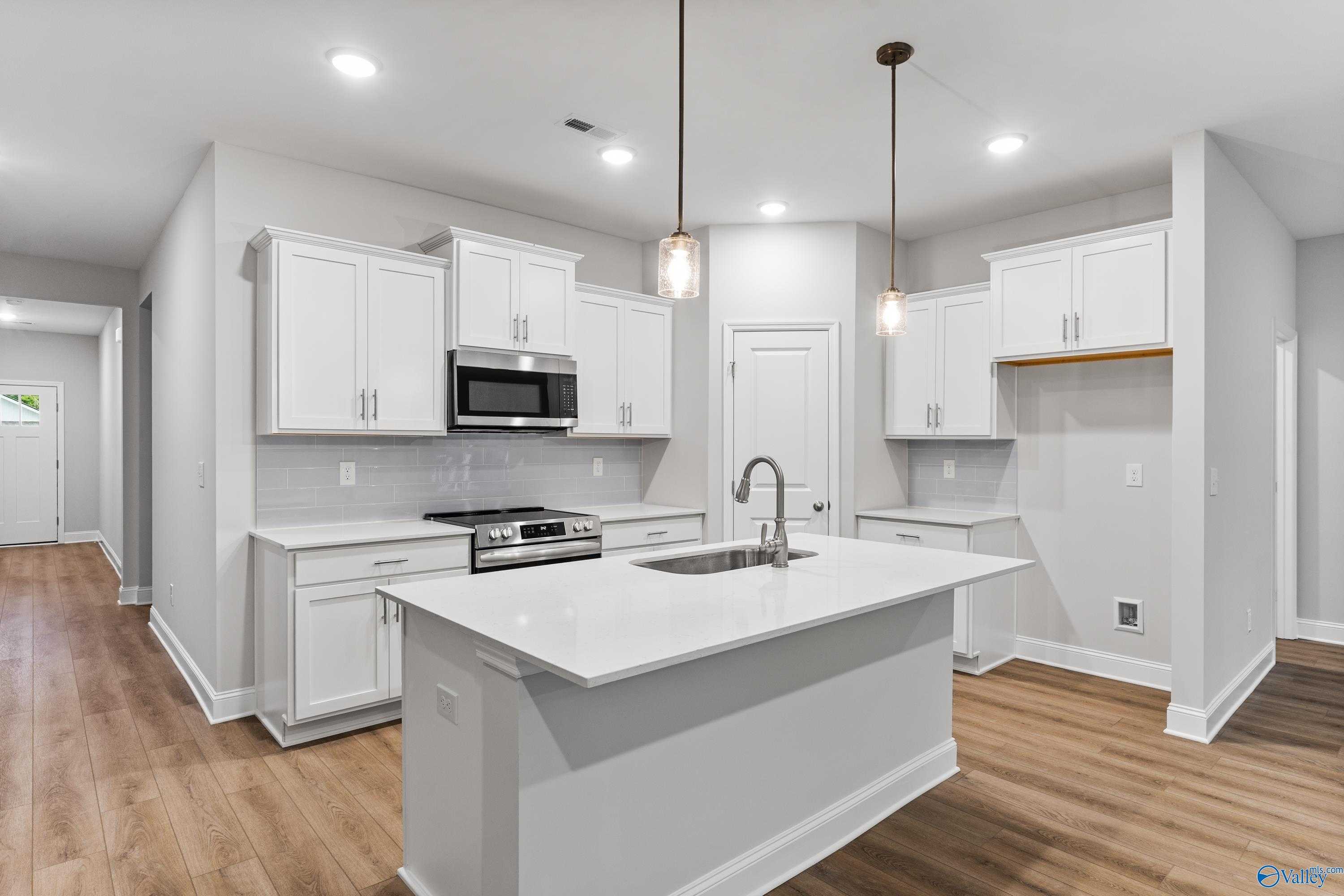 Modern white kitchen with stainless steel appliances, quartz island, and pendant lights in The Daphne floor plan, Huntsville, AL