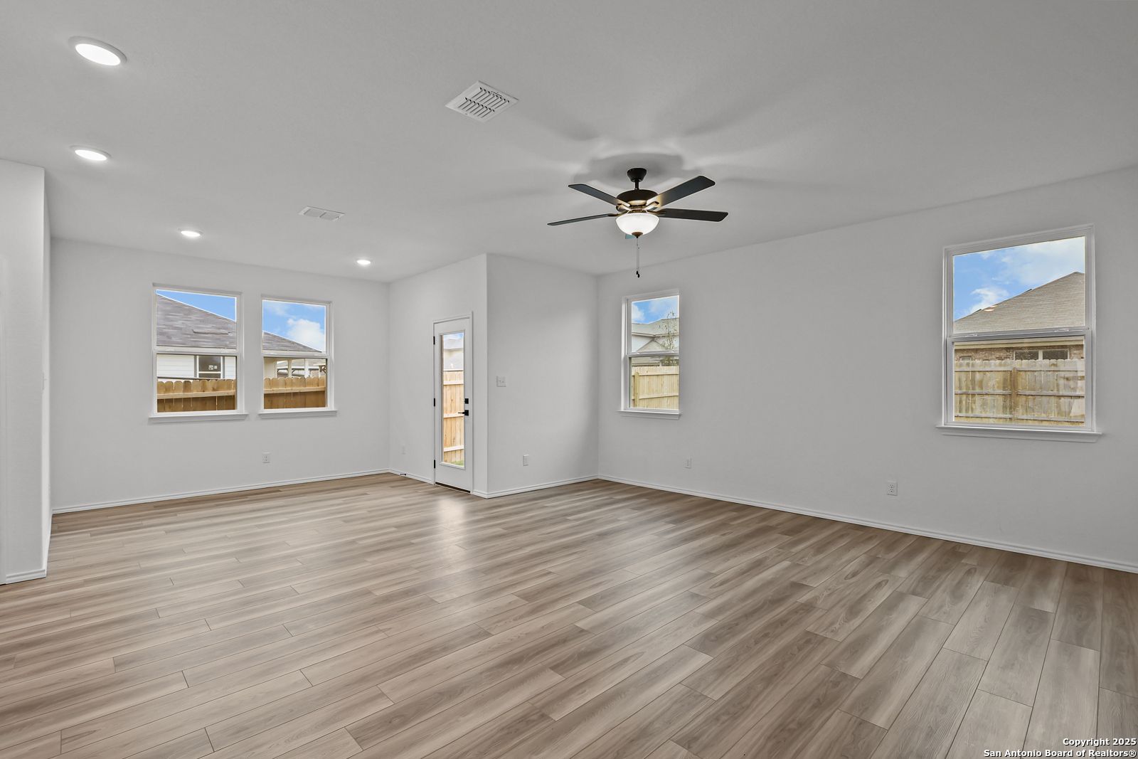 Bright open living room with hardwood floors, ceiling fan, recessed lights, and large windows in Davidson Homes The Daphne J, Converse, Texas