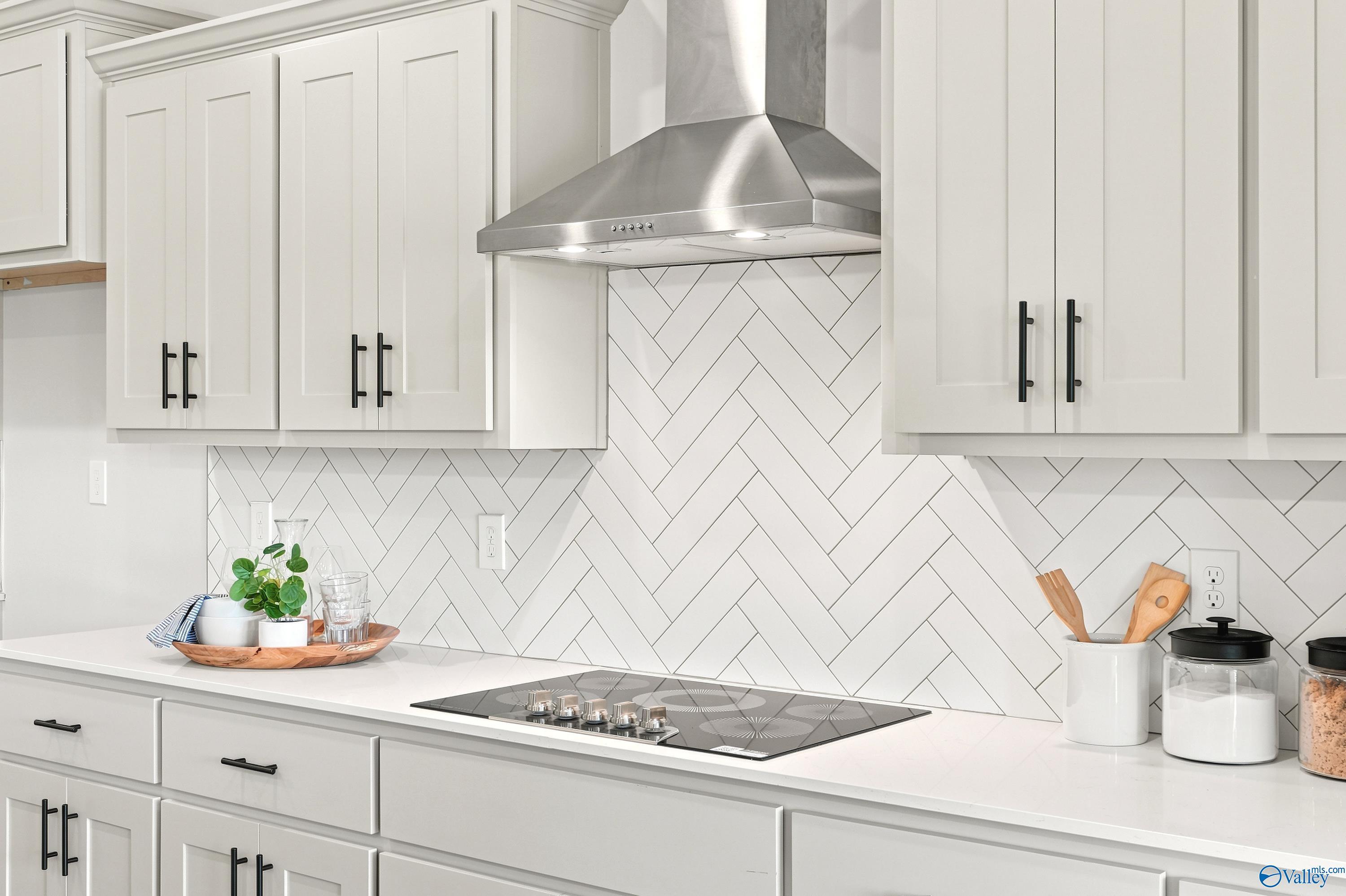 Modern kitchen with herringbone tile backsplash and stainless vent hood in The Finleigh, Riverton Preserve, Huntsville.