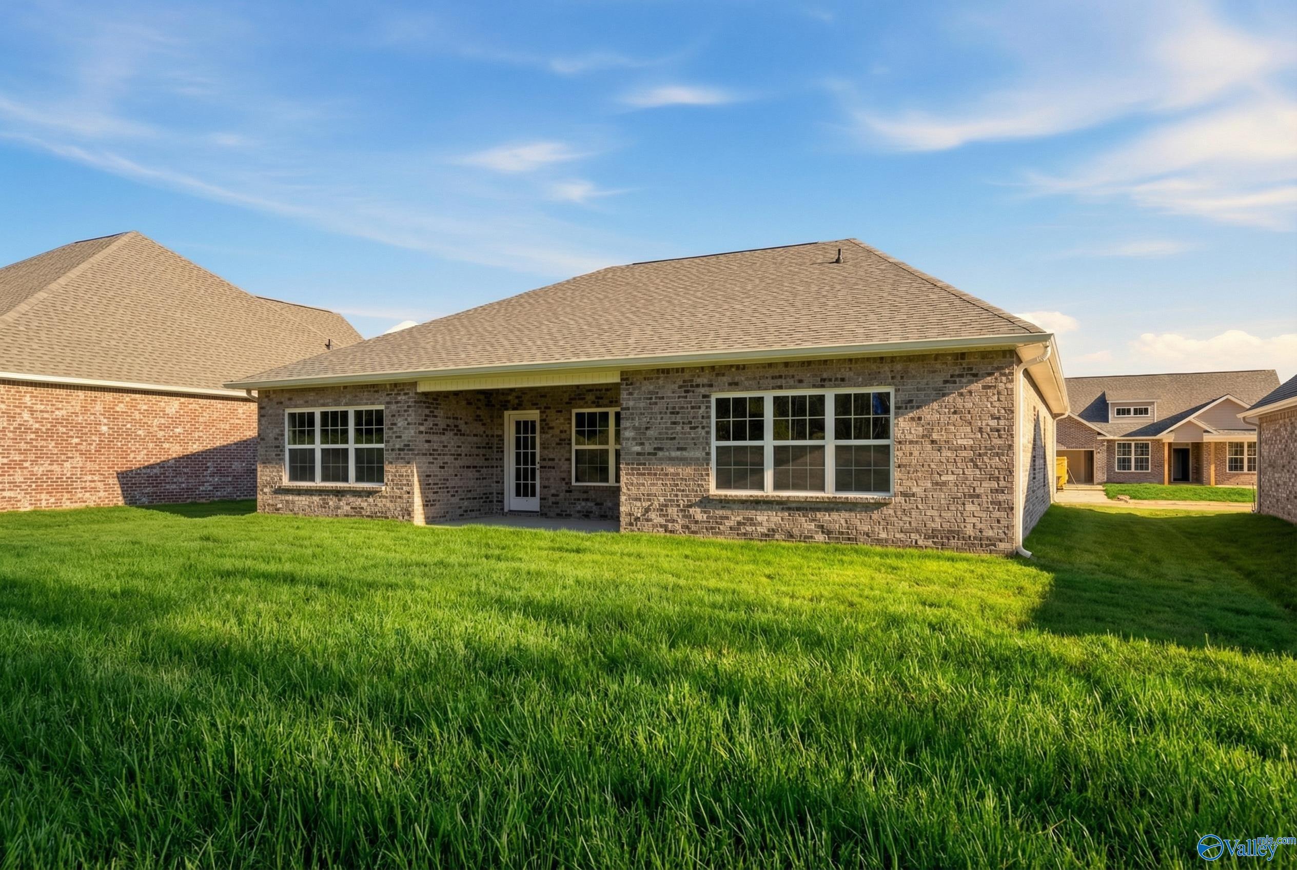 Brick single-story home exterior with covered porch, lush green lawn, and blue sky in Cain Park, Hartselle, Alabama - Davidson Homes The Montgomery