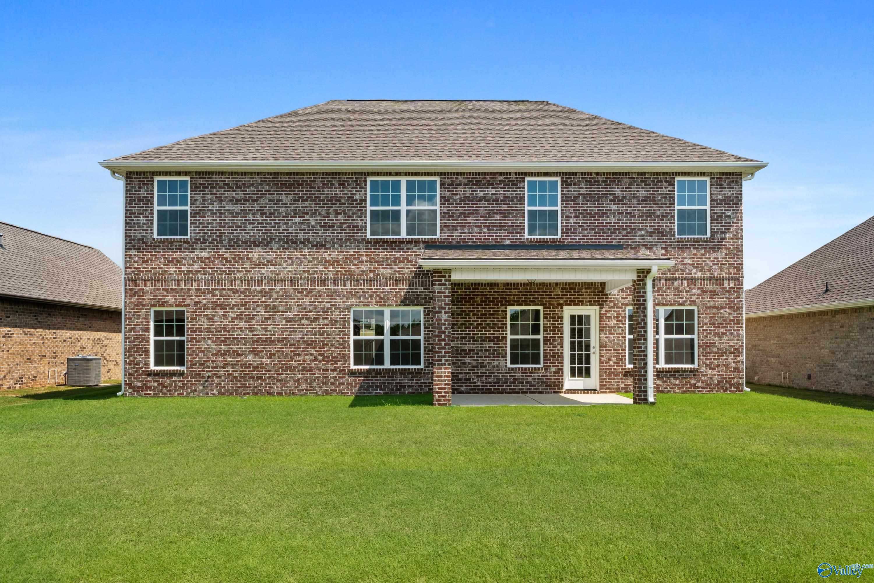 Rear view of two-story brick 5-bedroom home with covered patio, large windows, and green lawn in Kendall Downs, Toney, Alabama